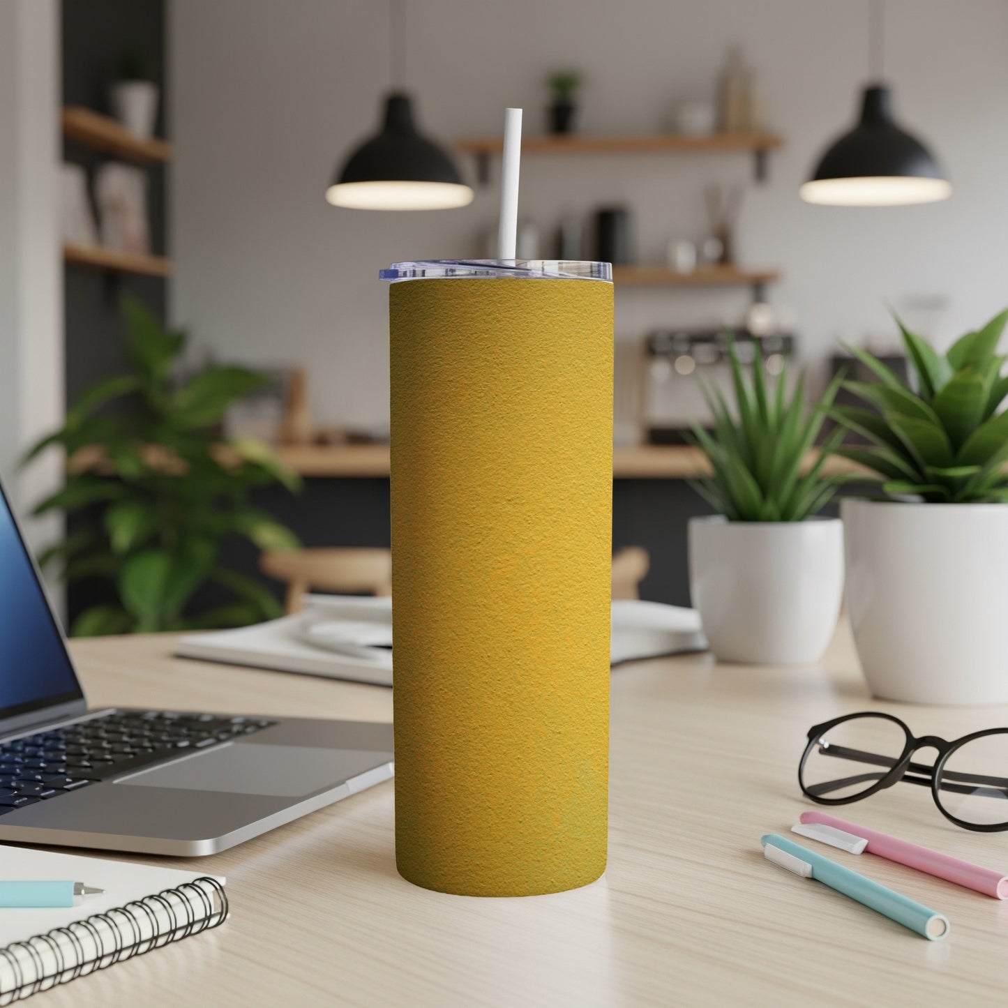 Yellow textured tumbler with white straw on a desk with laptop and pens.
