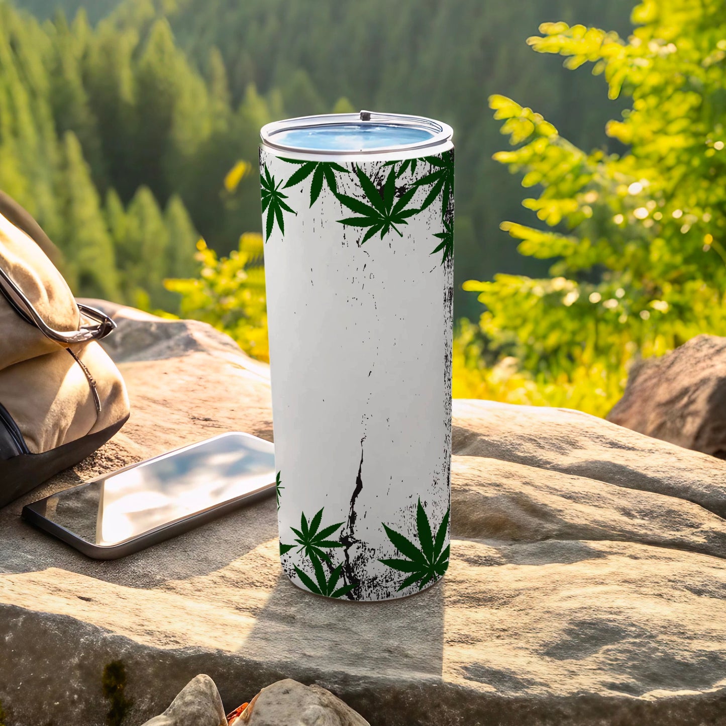 White tumbler with green cannabis leaf design, outdoors.