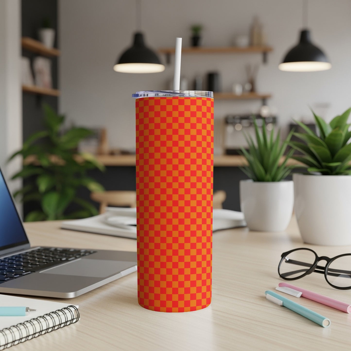 Orange and red checkered tumbler with straw on desk.