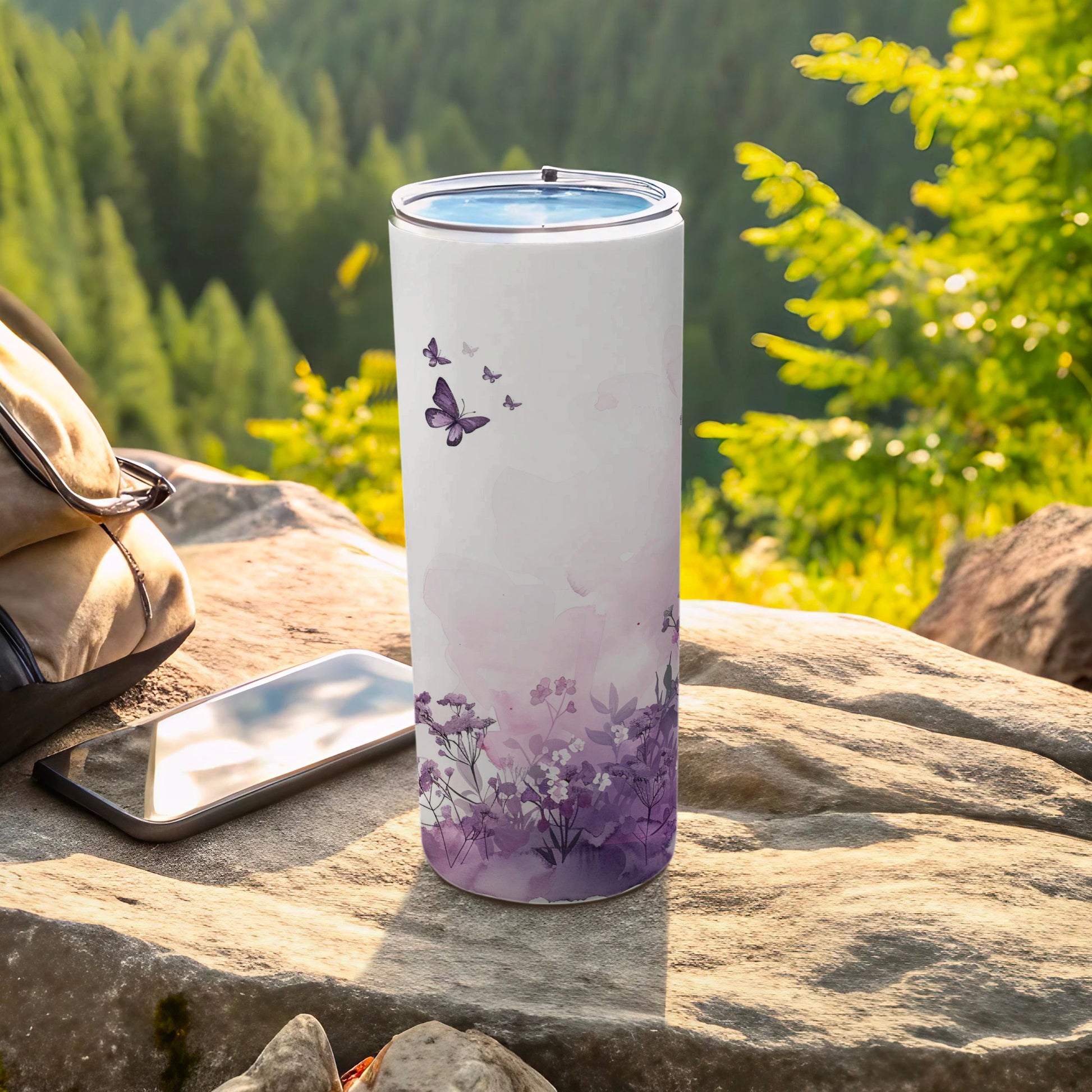 White tumbler with purple floral and butterfly design on outdoor rock setting.