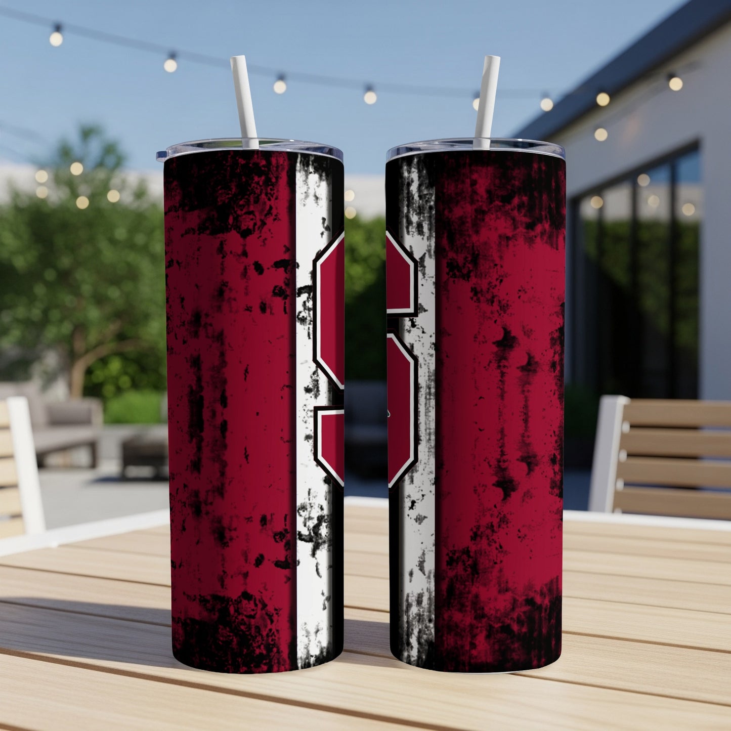 Two red and white distressed tumblers with straws sit on a wooden table outside.