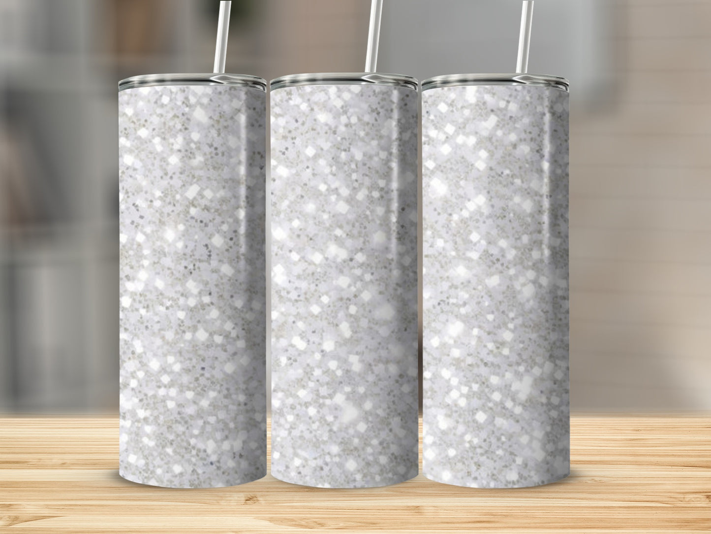 Three glittery tumblers with straws on a wooden surface.