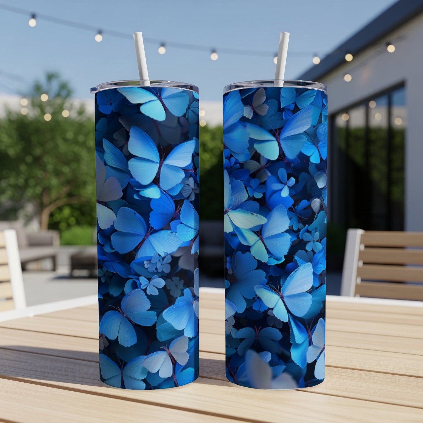 Two blue butterfly patterned tumblers with straws on a wooden table outdoors.