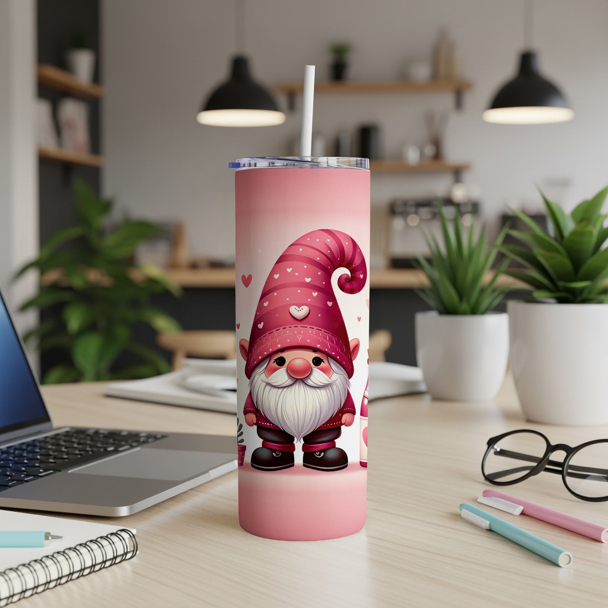 Pink gnome tumbler with hearts and a straw, on a desk.