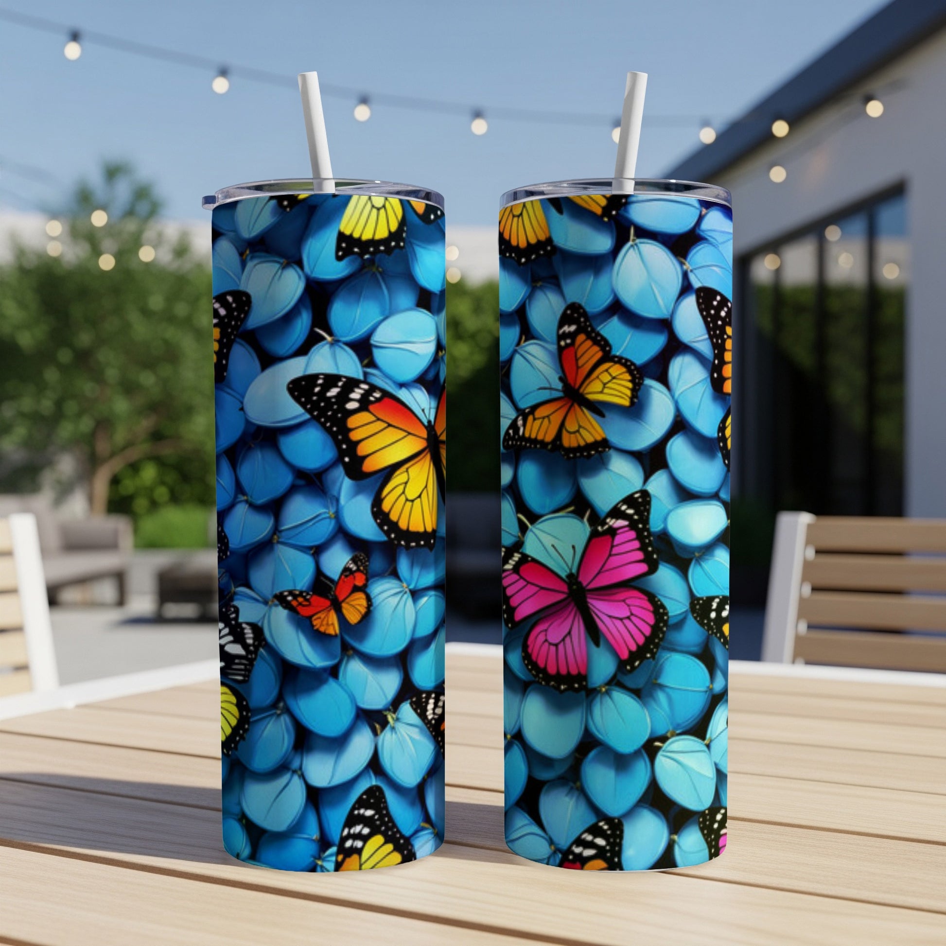 Two blue tumblers with colorful butterflies and straw against an outdoor background.