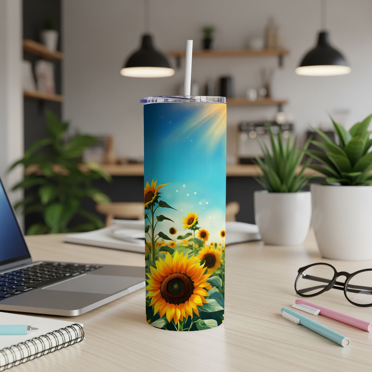 Sunflower tumbler with straw on a desk with a laptop and plants.