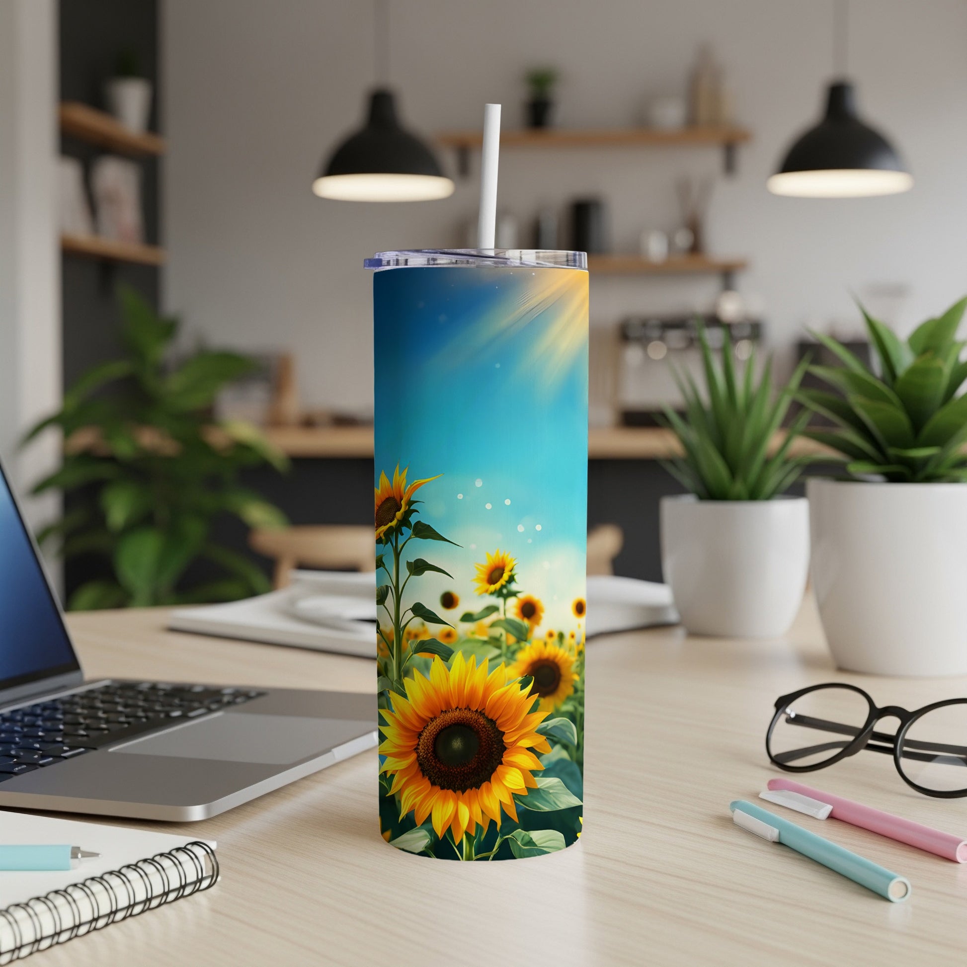 Sunflower tumbler with straw on a desk with a laptop and plants.