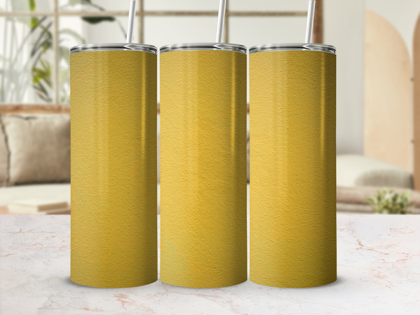 Three gold textured tumblers with straws sit on a marble surface.