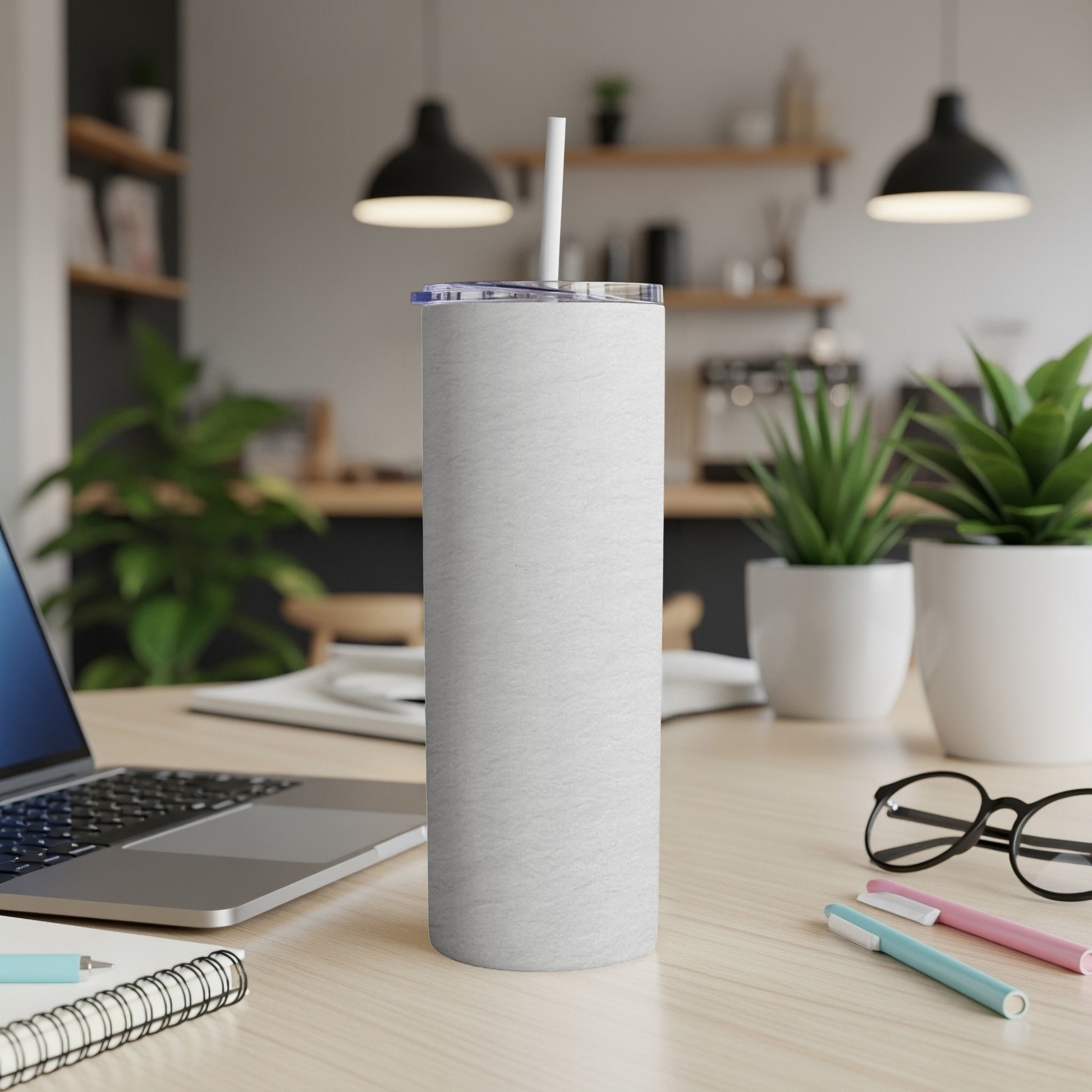 White tumbler with straw on a desk next to a laptop and pens.