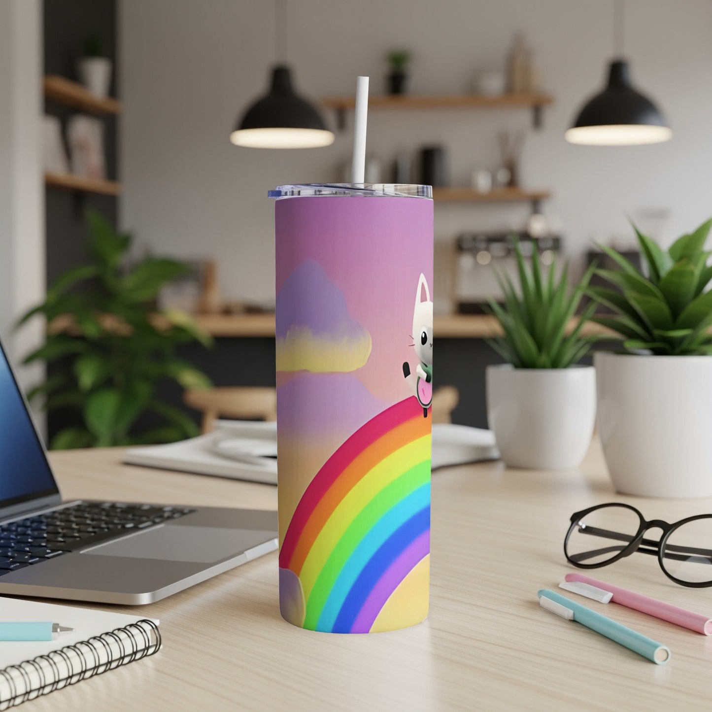 White cat on a rainbow design tumbler with straw, on a desk.