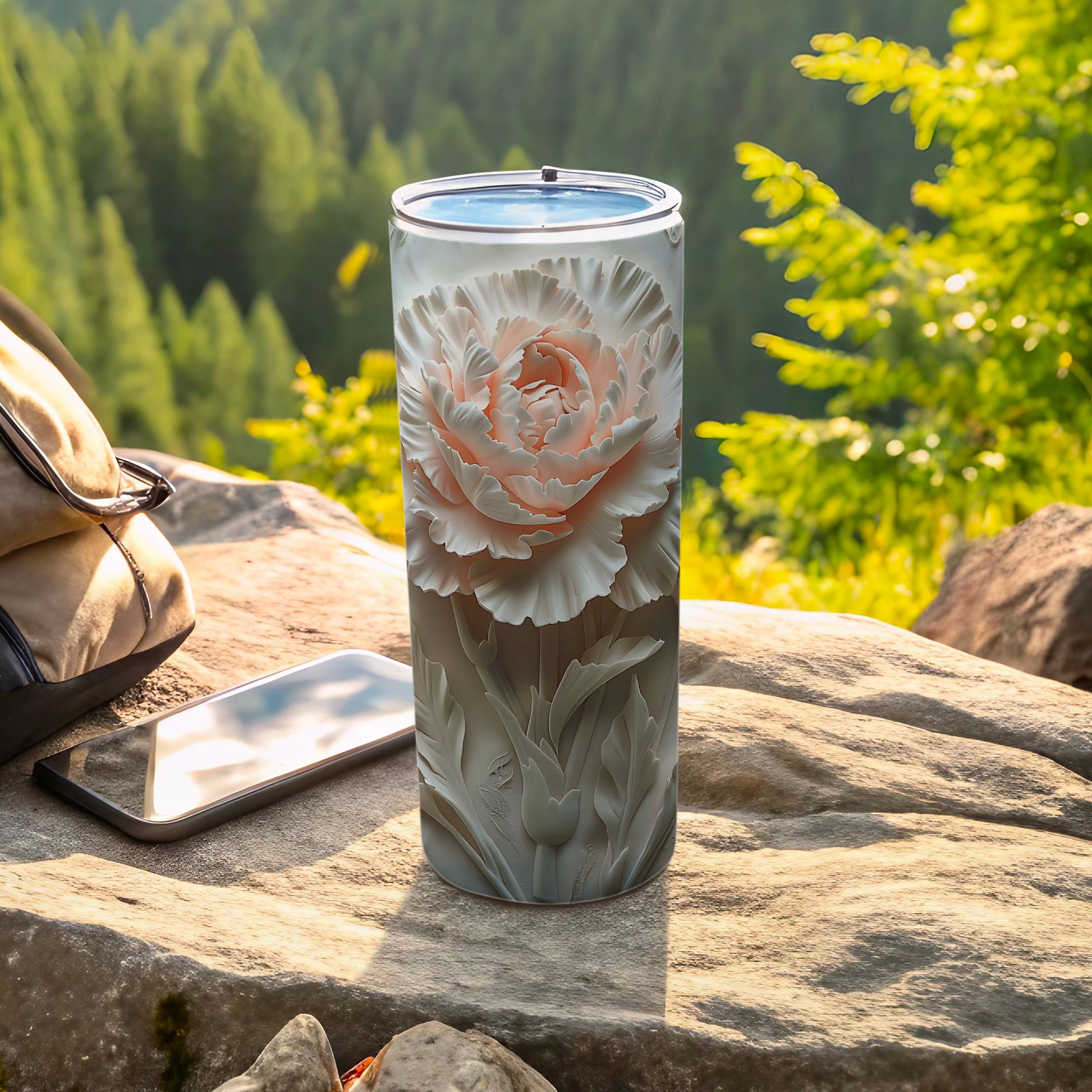White floral patterned tumbler on rock with phone and backpack.