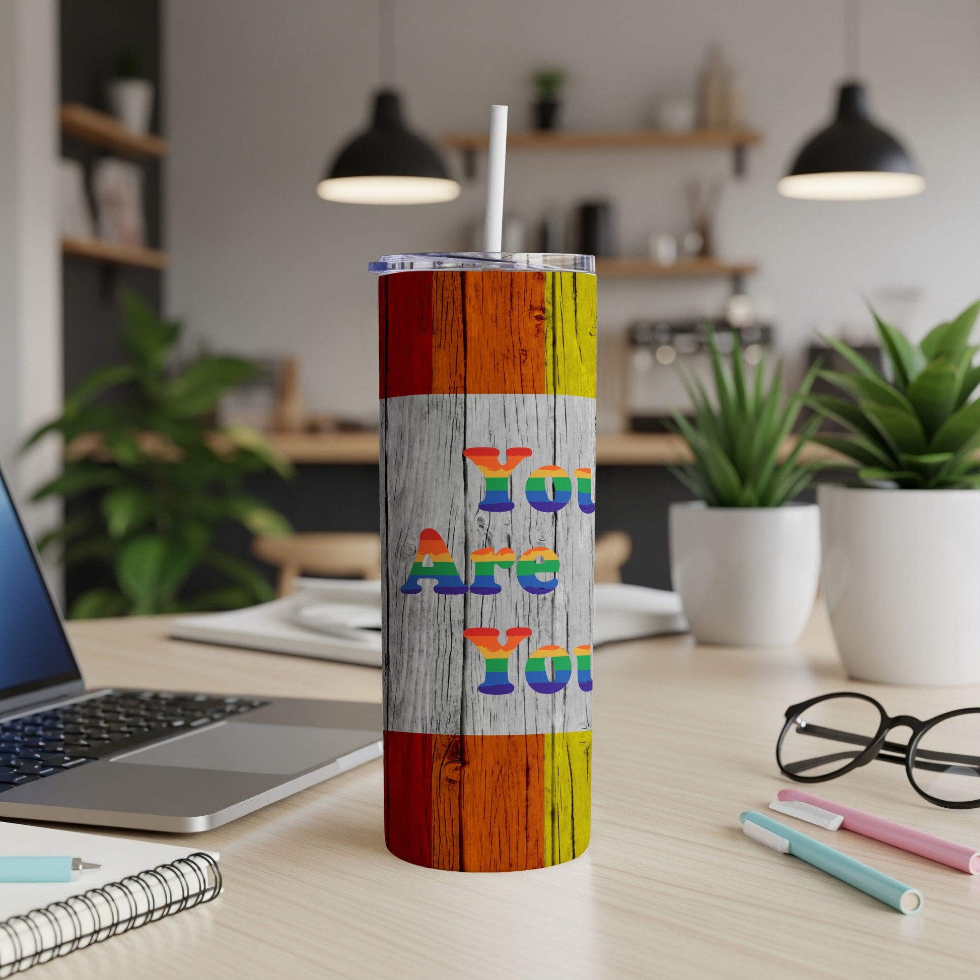 Rainbow stripe tumbler with "You Are You" text on a wooden desk.