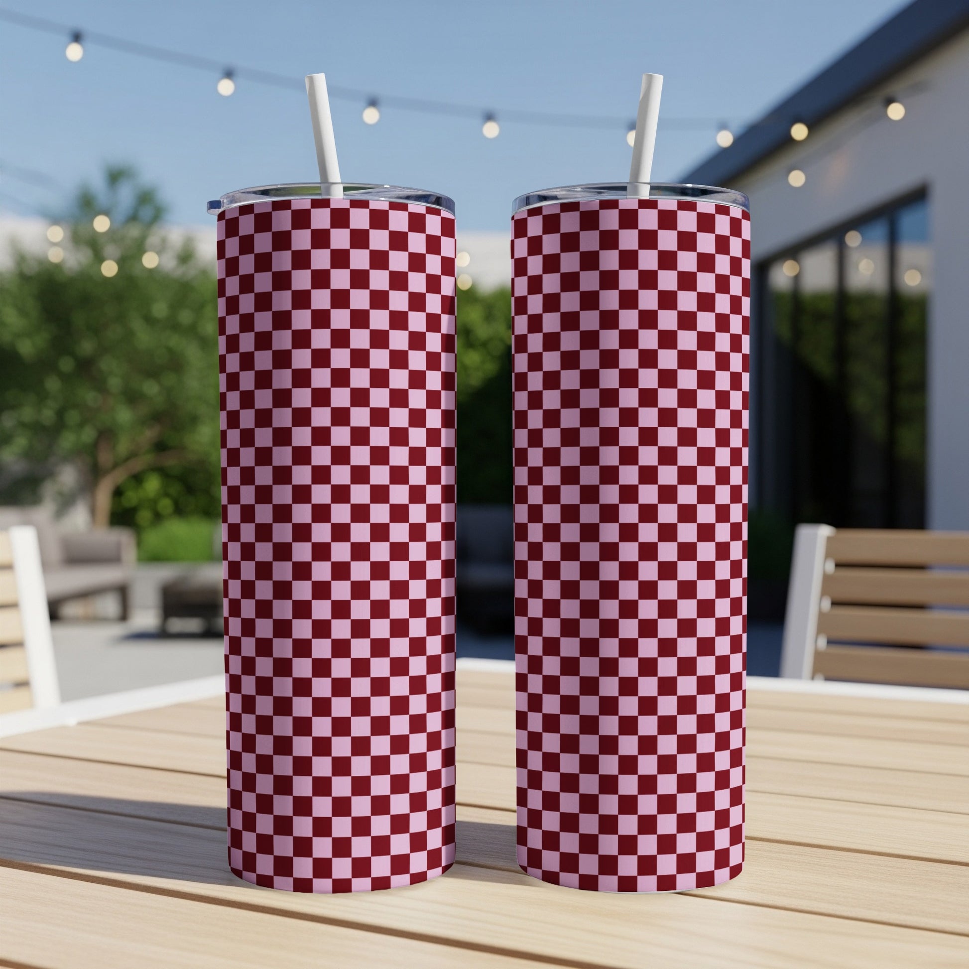 Two burgundy and pink checkered tumblers with straws on a wooden table.