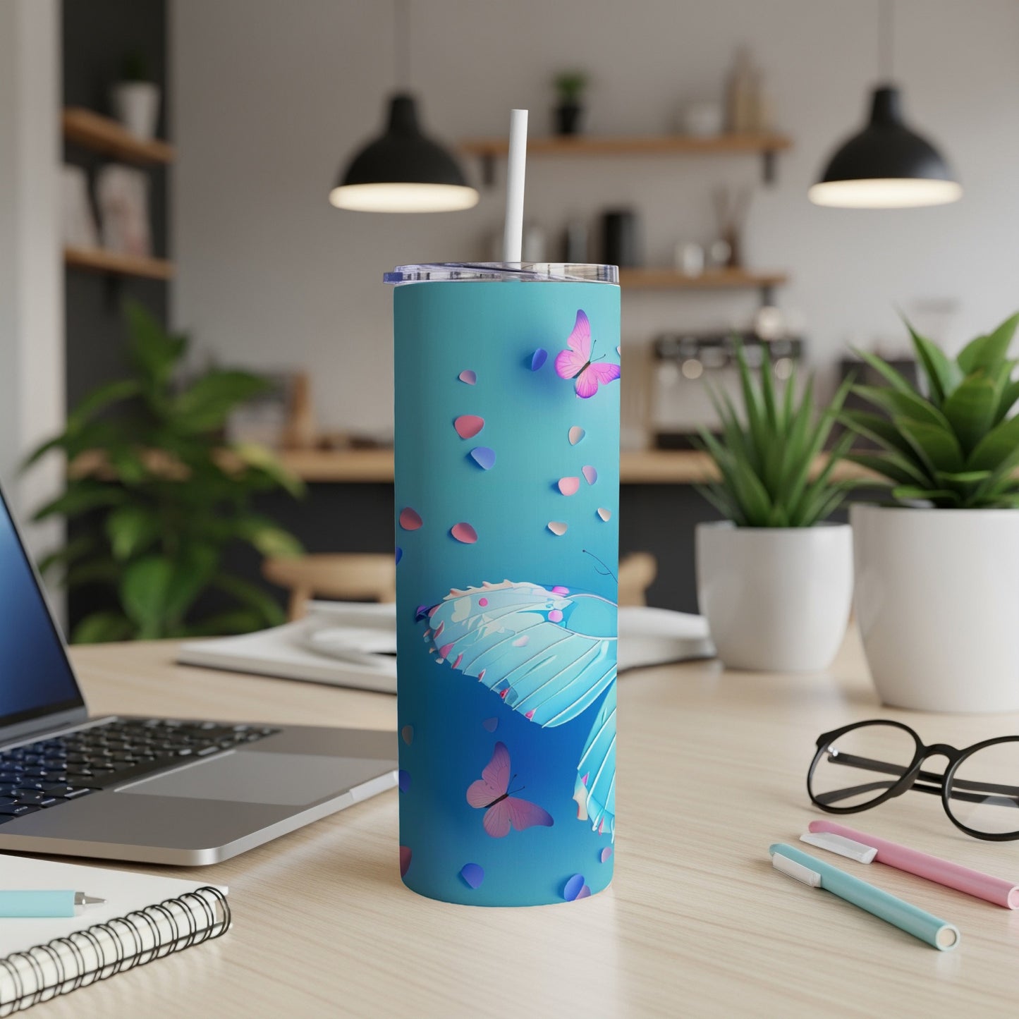 Turquoise tumbler with butterfly design and pink petals, on a desk.