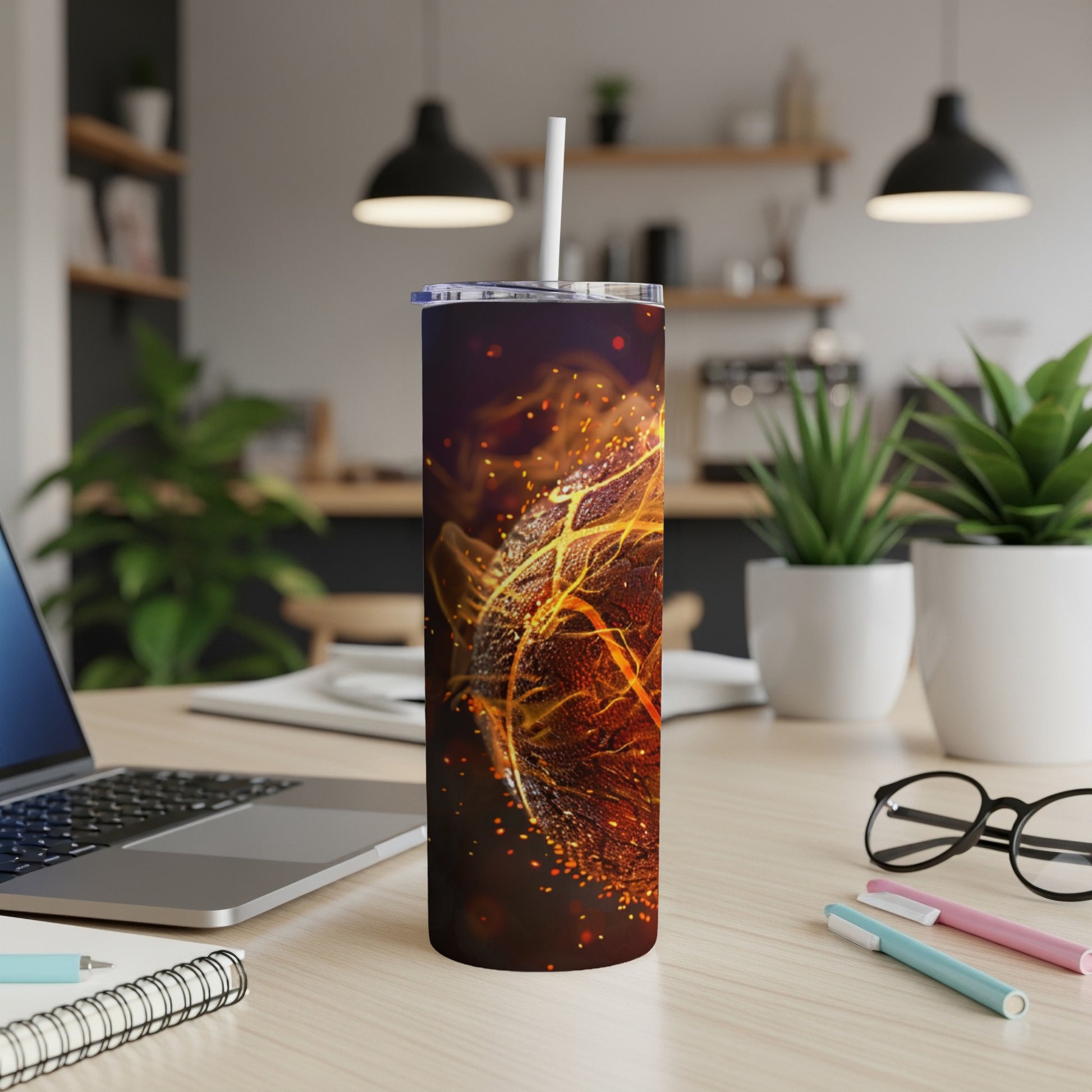 Tumbler with fiery, glowing leaf design on a desk with laptop.