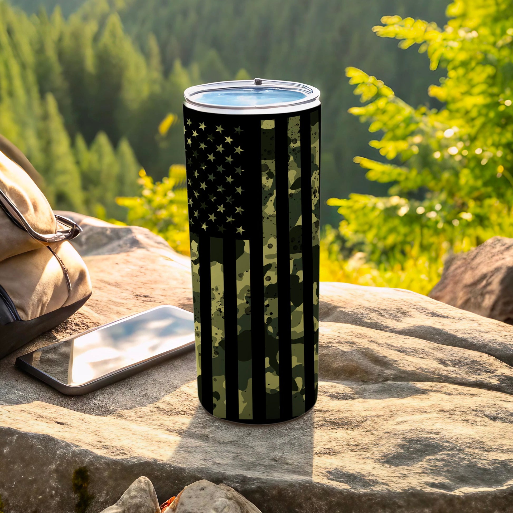 Camouflage American flag tumbler on rock with backpack and phone.