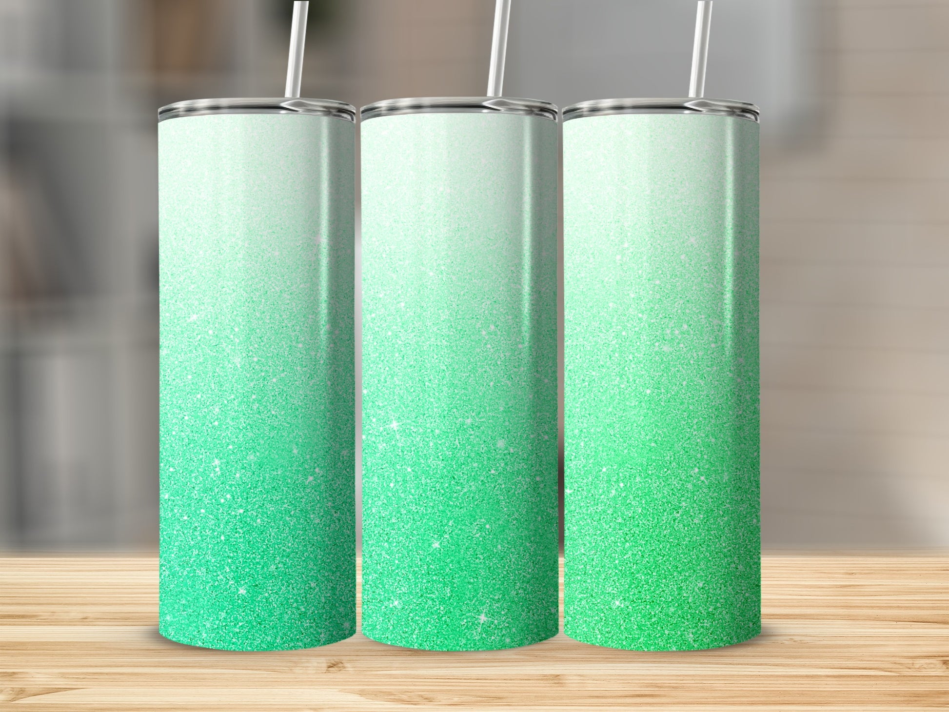 Three tall tumblers with a green glitter ombre design stand on a wooden surface.
