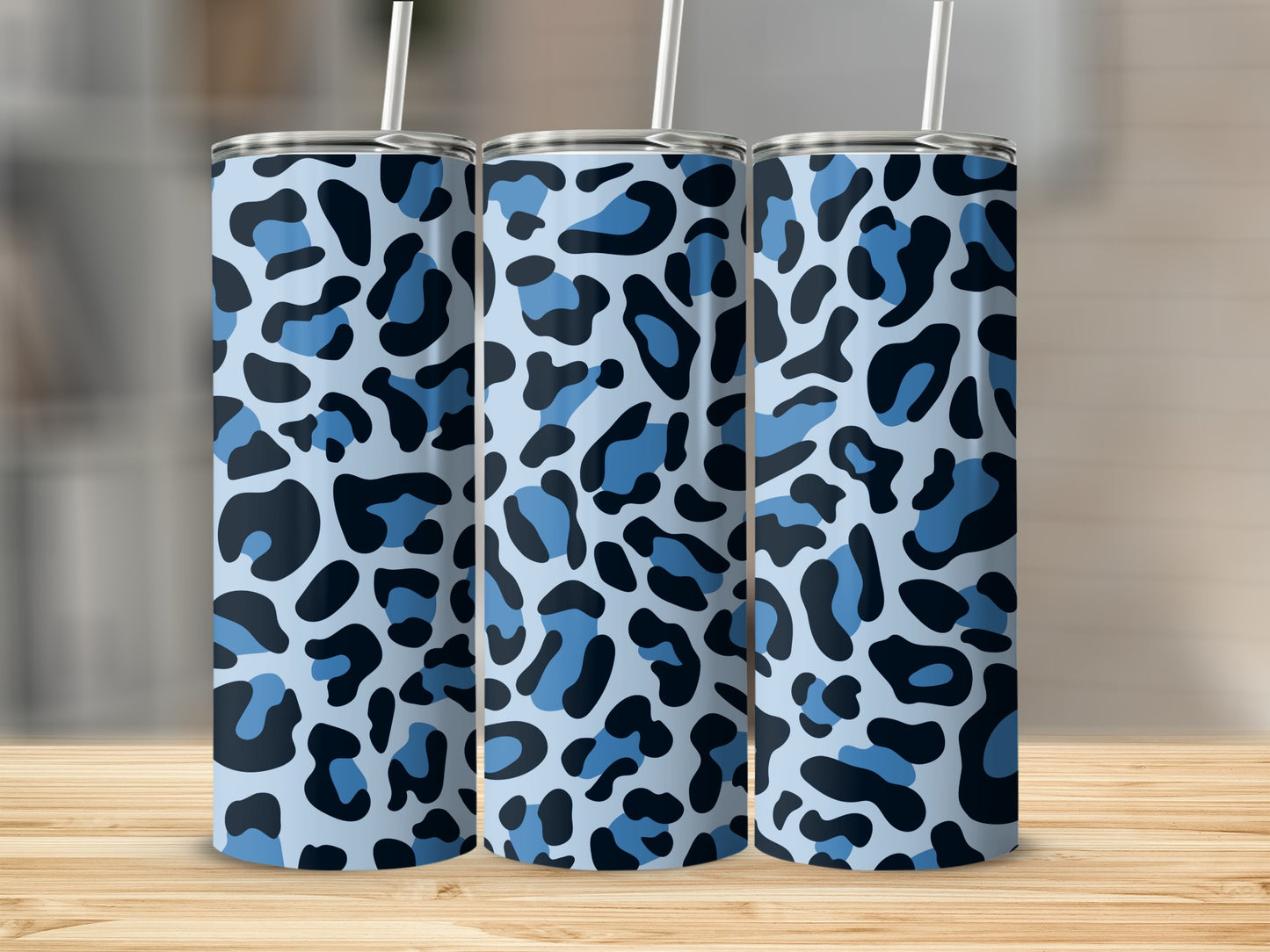 Three blue leopard print tumblers with white straws on a wooden surface.