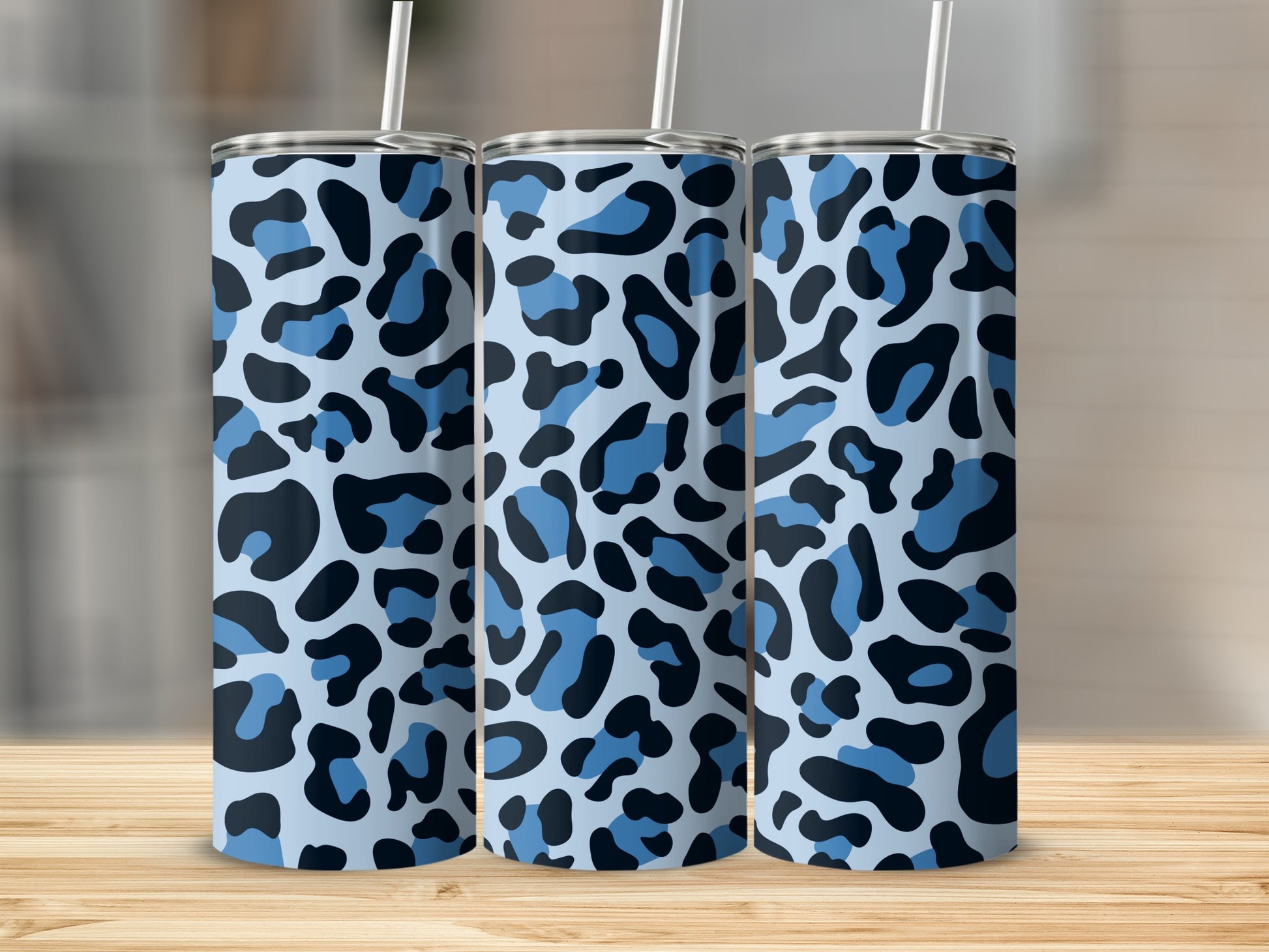 Three blue leopard print tumblers with white straws on a wooden surface.