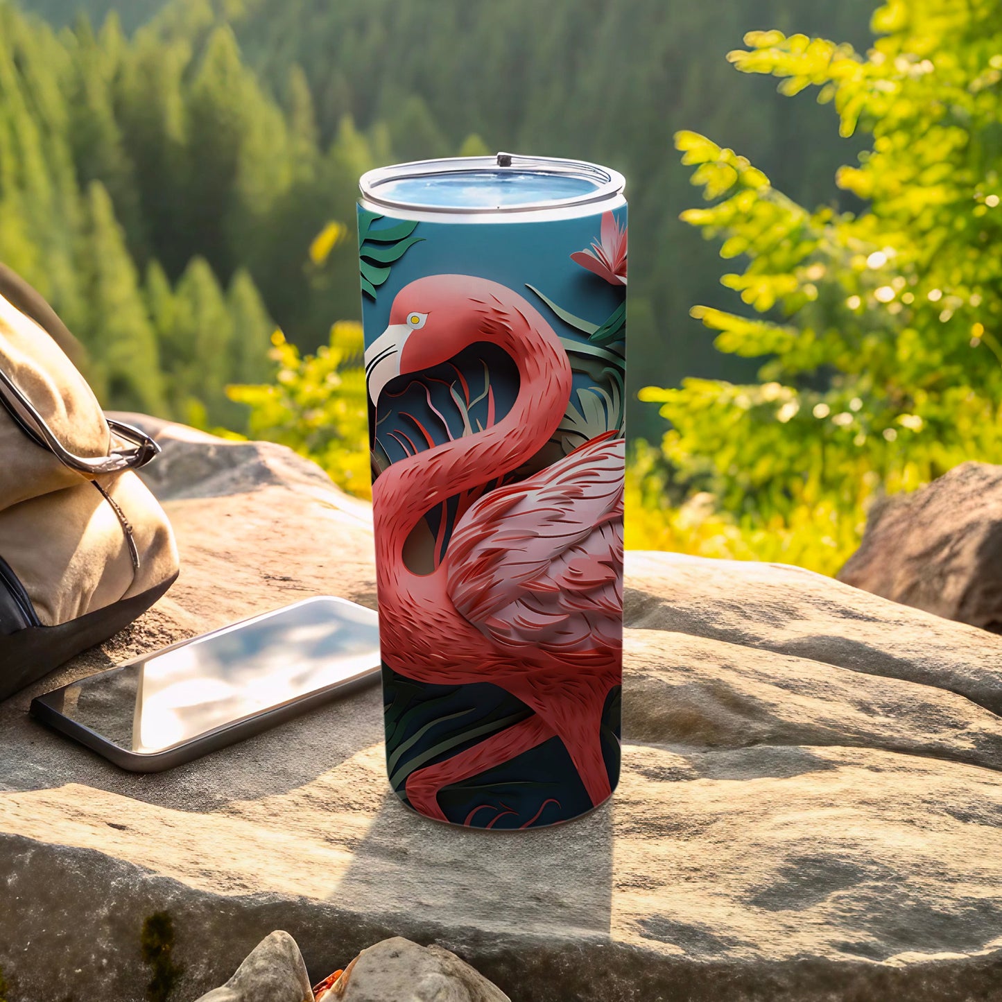 Flamingo design tumbler with tropical leaves, on rocks outdoors.