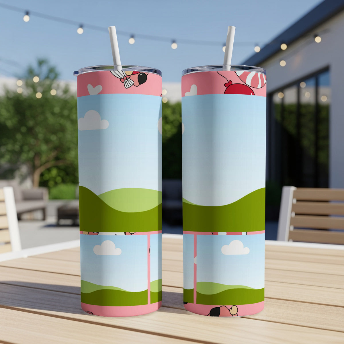 Two tumblers with a cartoon landscape and balloon design sit on a wooden table.