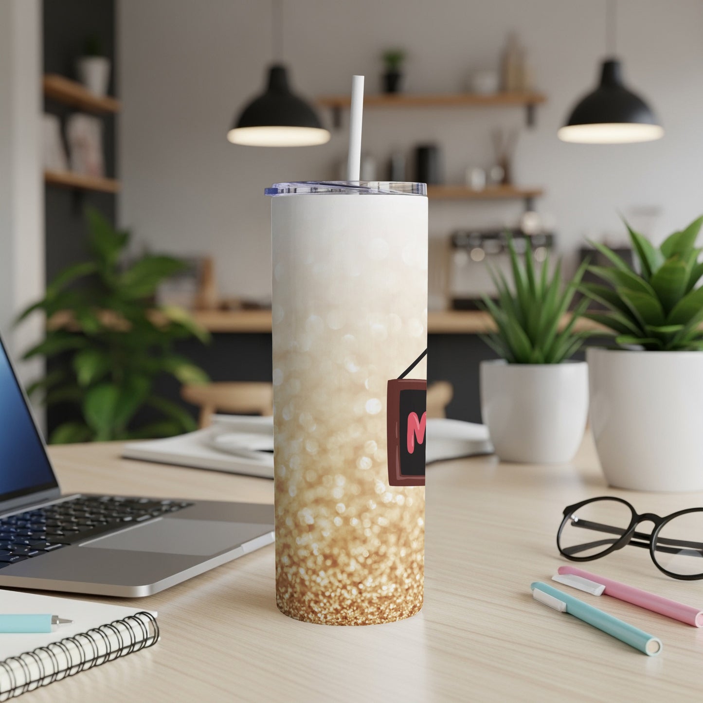 Glittery tumbler with "Mom" sign on a desk with a laptop and pens.