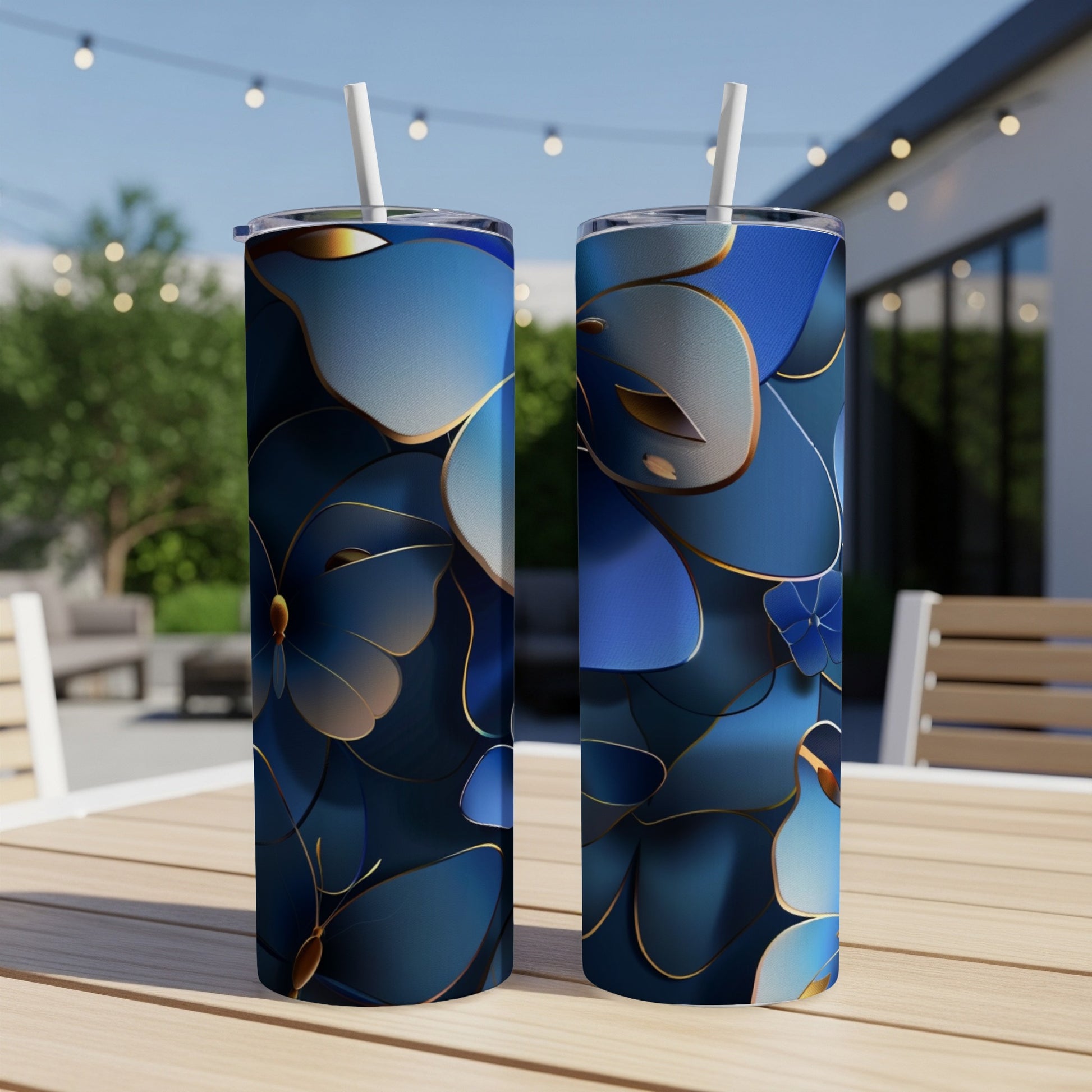 Two blue floral tumblers with gold trim and straws on a patio table.