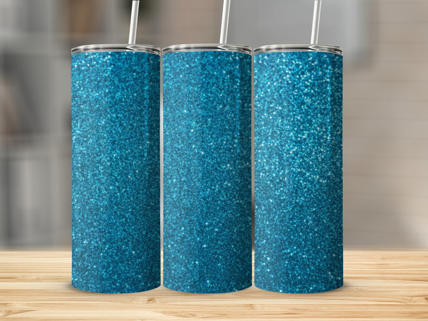 Three sparkly blue glitter tumblers with white straws on a wooden surface.