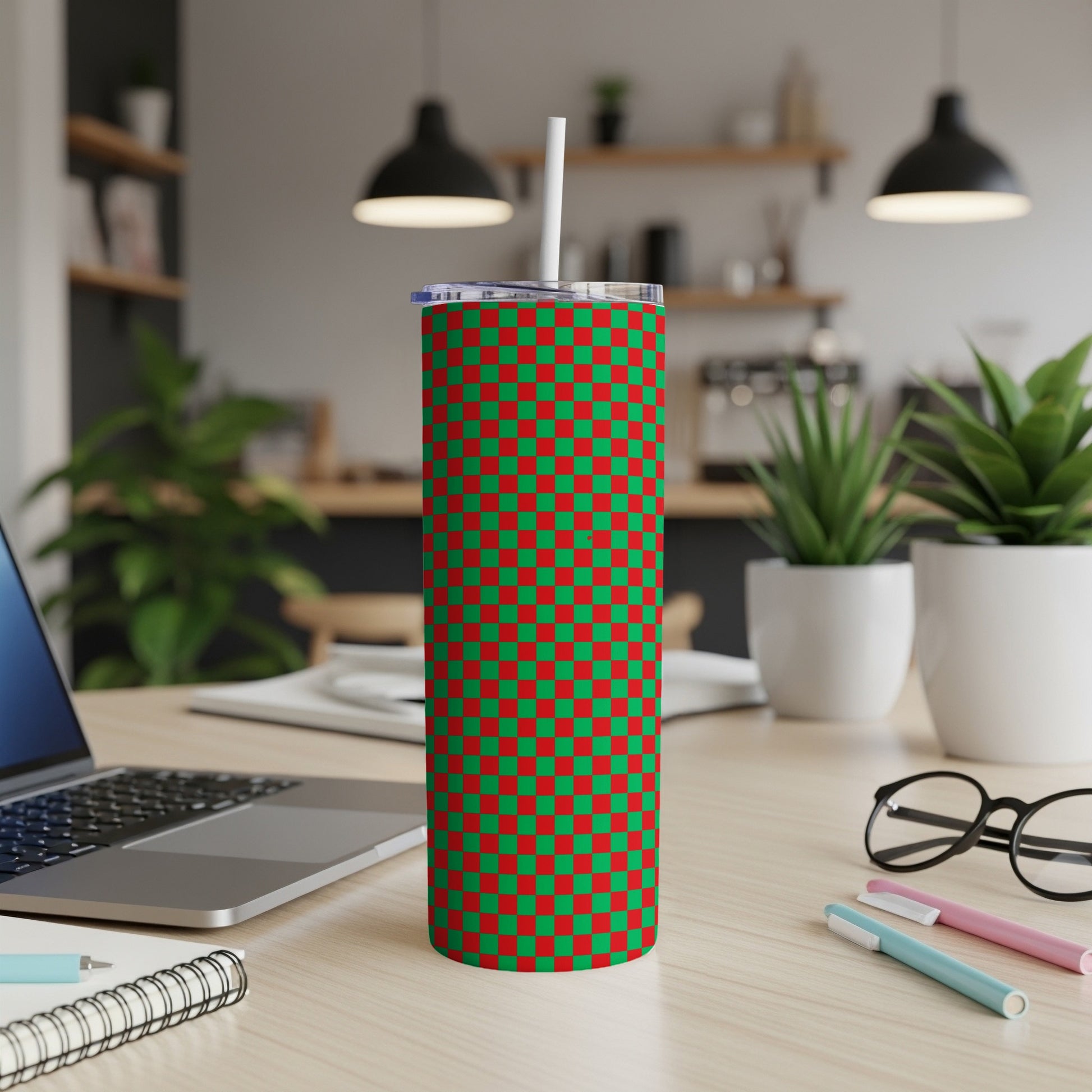 Green and red checkered pattern tumbler with straw on a desk.