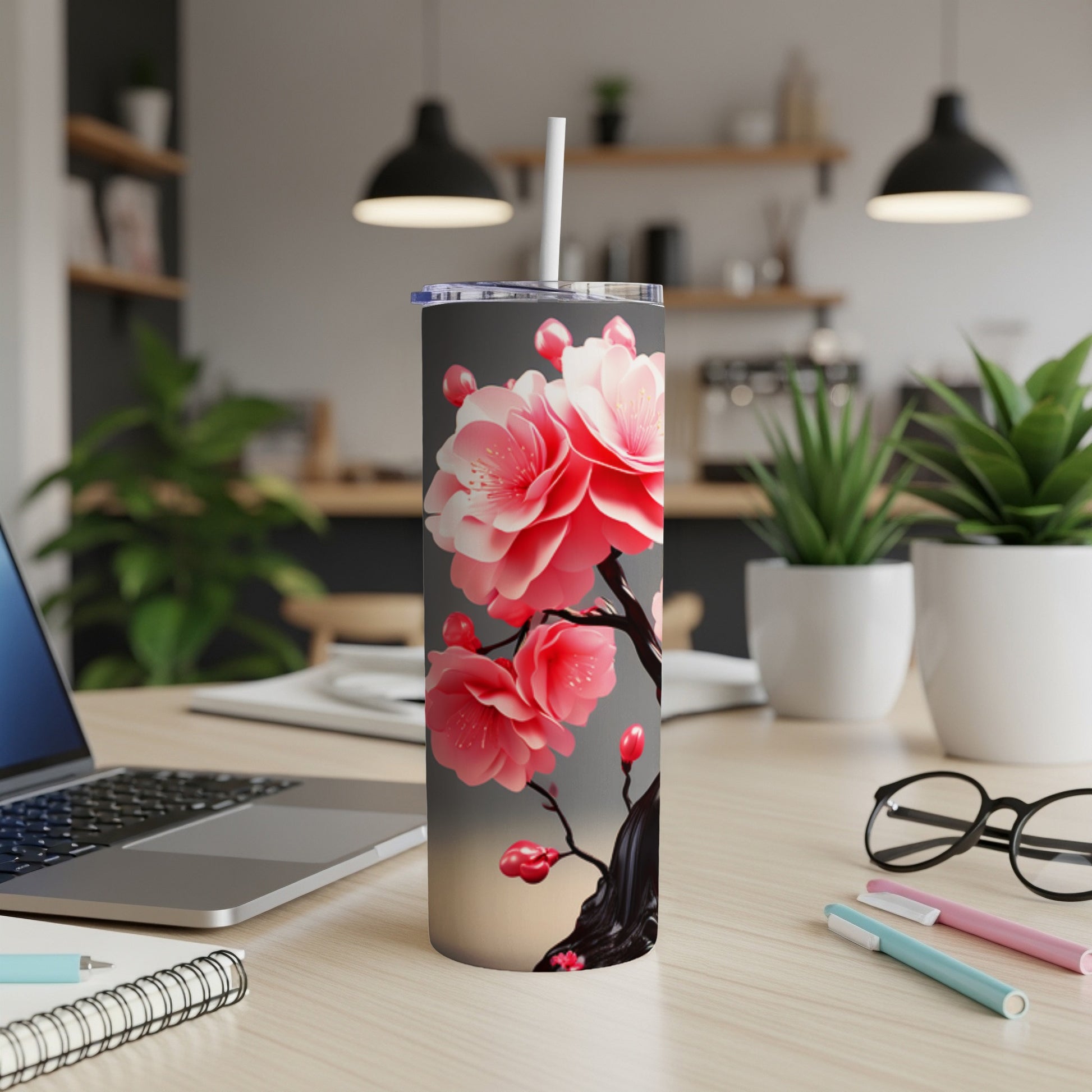 Pink cherry blossoms on a grey tumbler with straw on a desk.