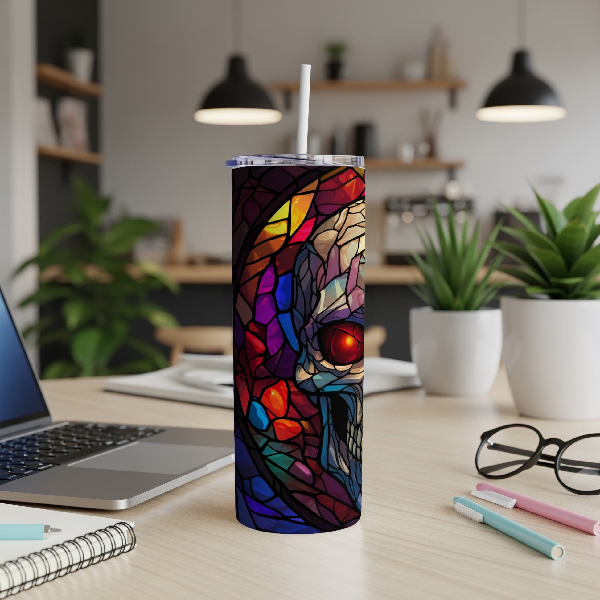 Stained glass skull tumbler with straw on a desk next to a laptop.
