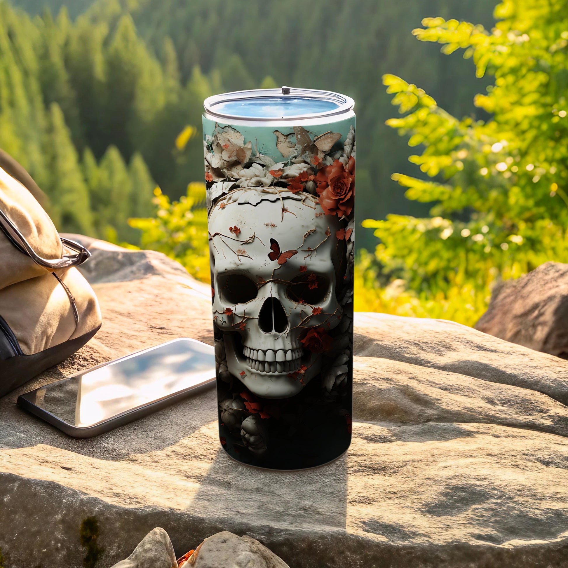 Tumbler with skull and floral design on rocky outdoor surface.