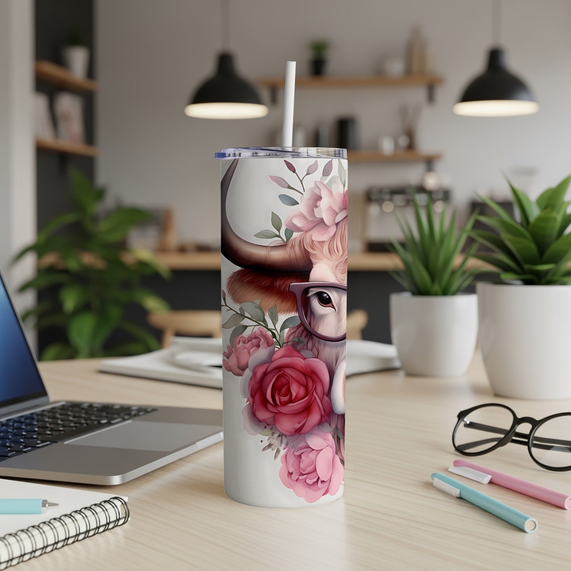 Cow with glasses and roses on a tumbler, with a laptop and pens in the background.