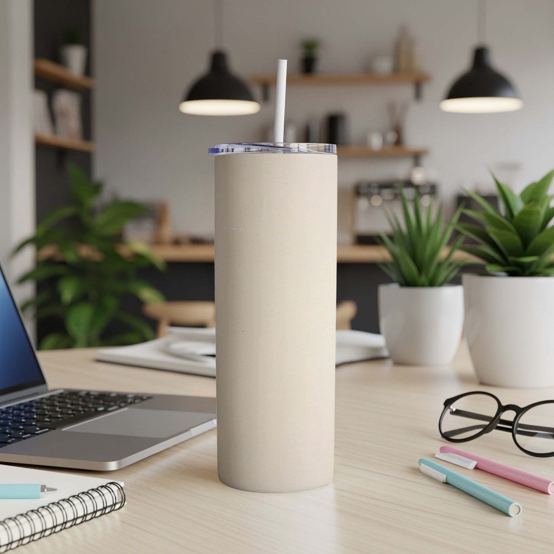 Cream colored tumbler with straw on a desk with a laptop.
