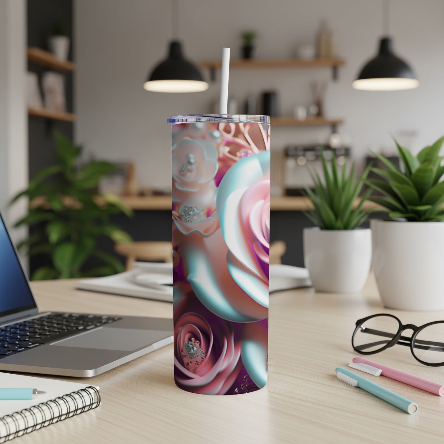 Tall tumbler with iridescent floral design and straw, on a desk.