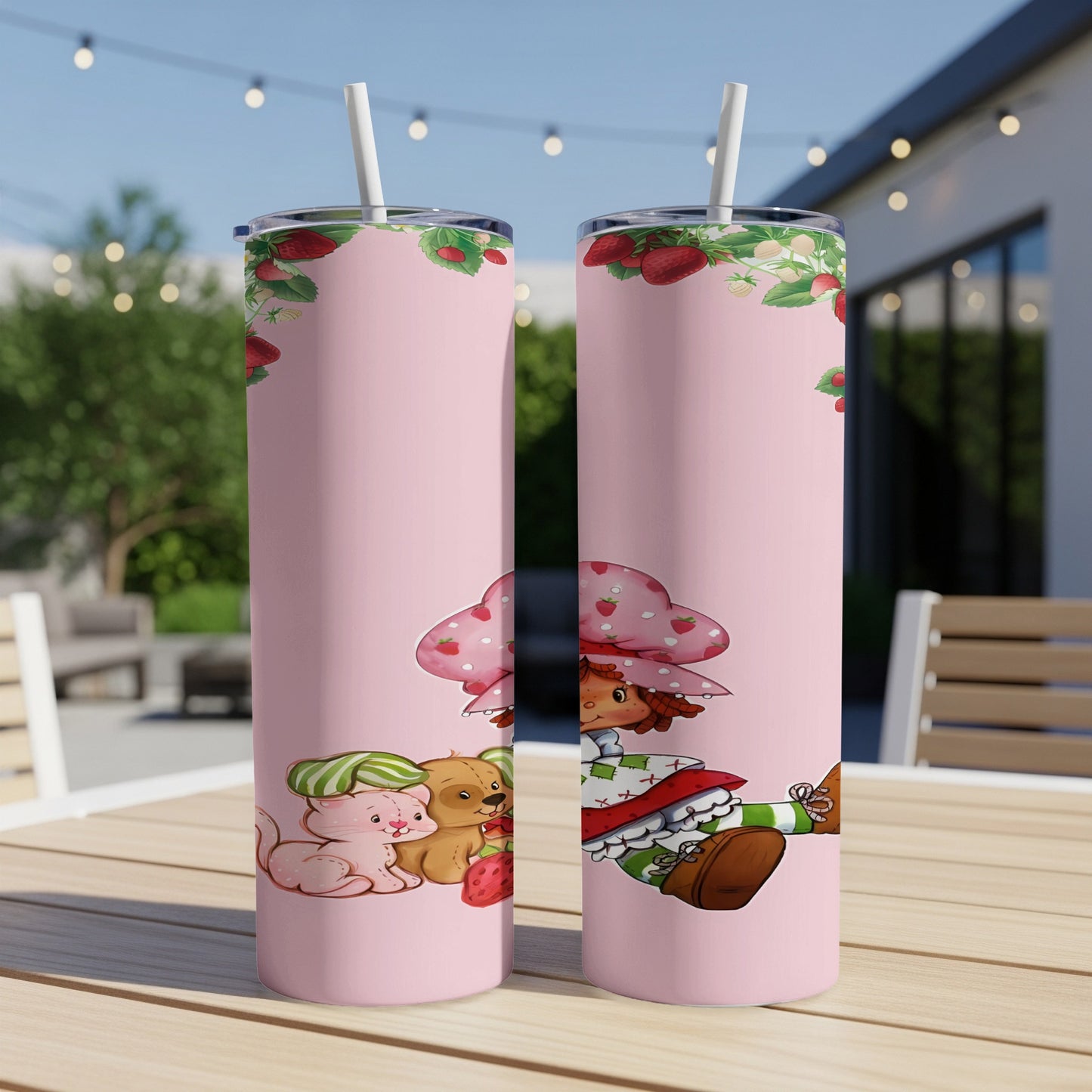 Two pink tumblers featuring Strawberry Shortcake and her friends on a patio table.