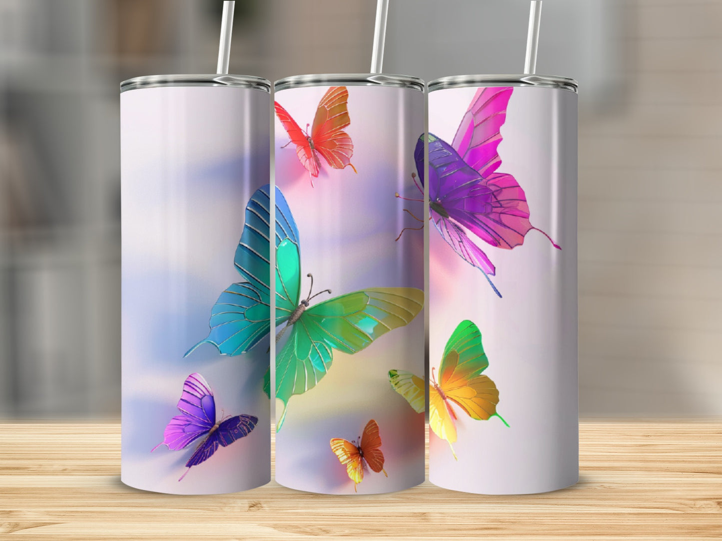 Three colorful butterfly tumblers with straws on a wooden surface.