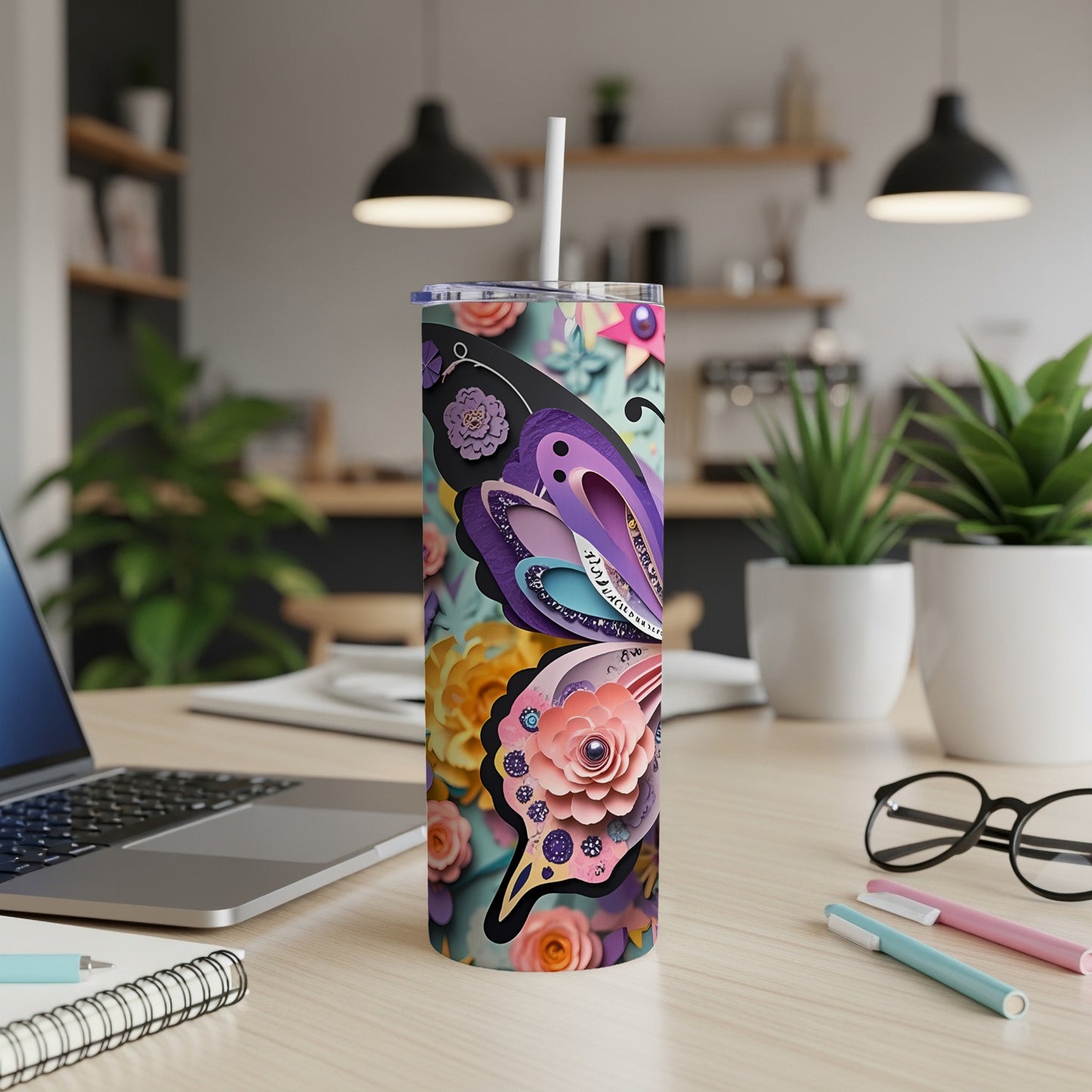Tumbler with butterfly and floral design, featuring a straw, on a desk.