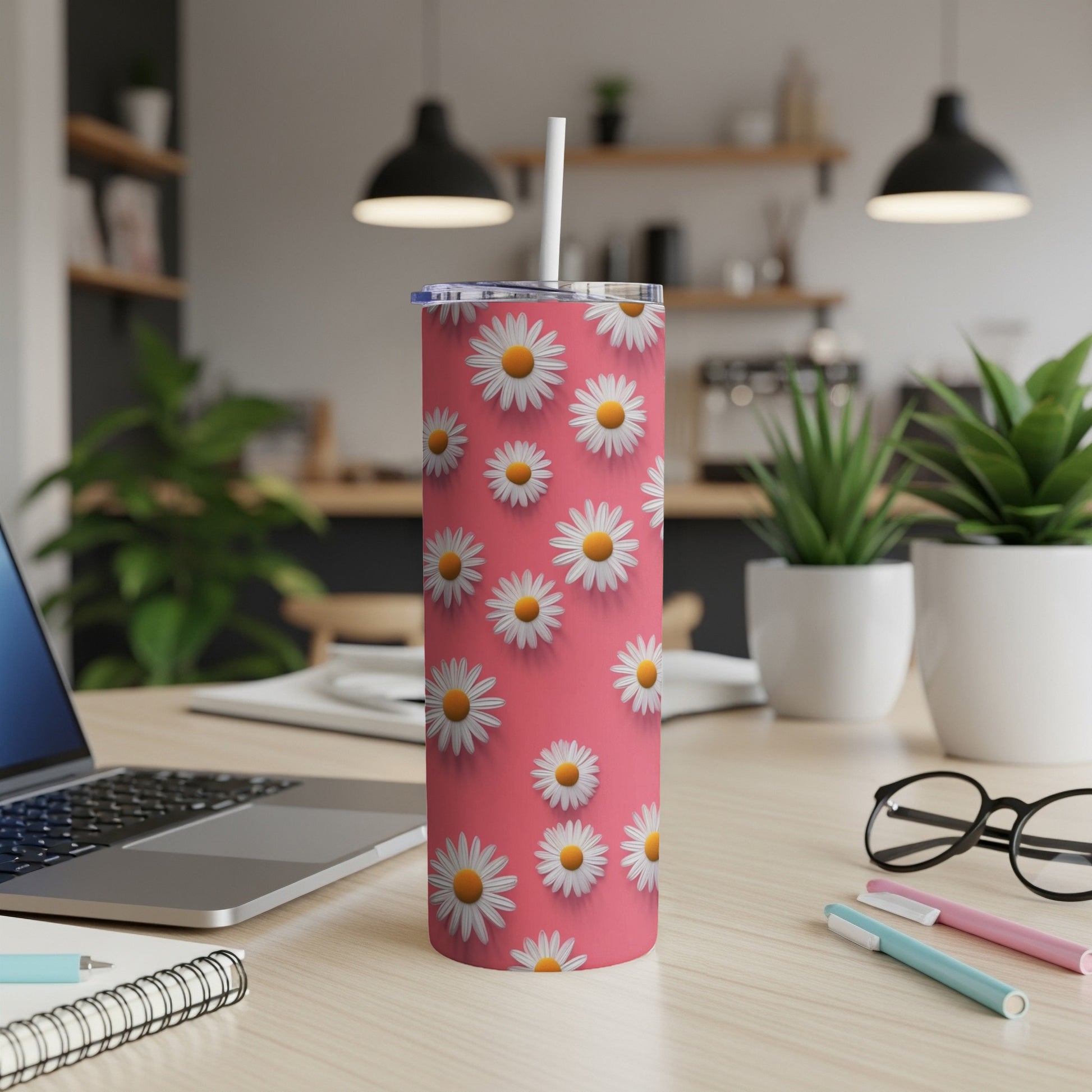 Pink tumbler with white daisy pattern and straw, on a desk.