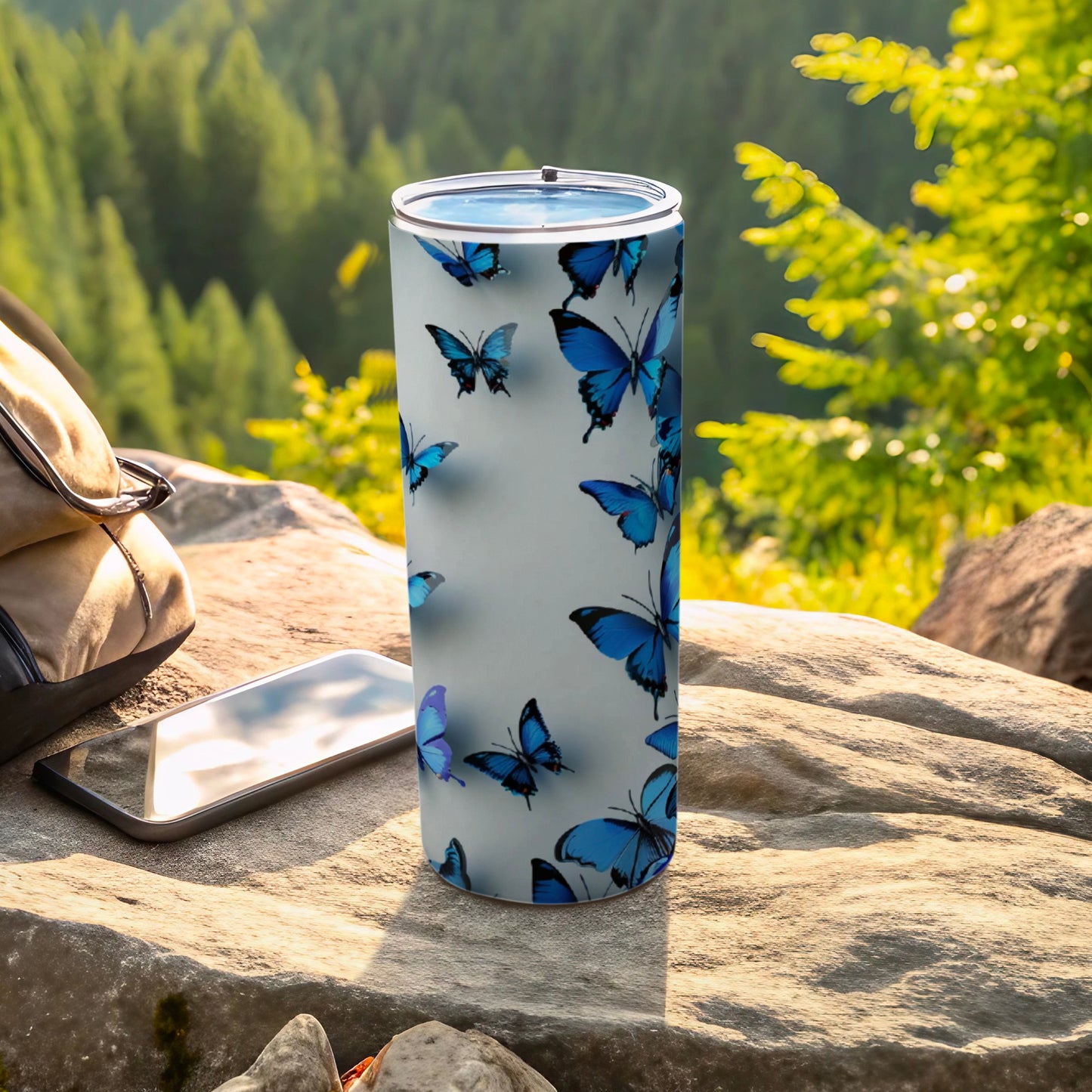 White tumbler with blue butterflies, rests on rocks outdoors.