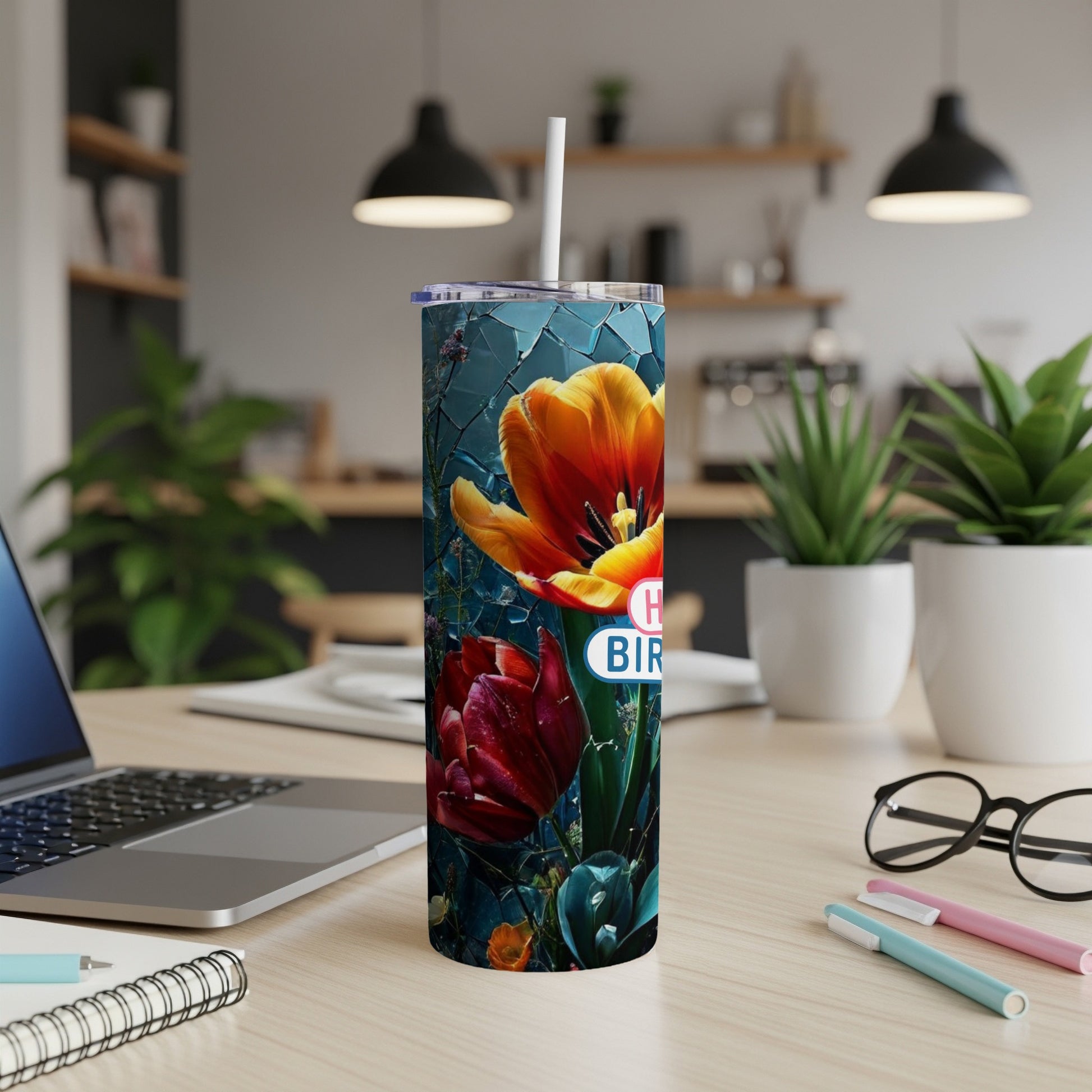 Floral tumbler with "Happy Birthday" text, on a desk with laptop and pens.