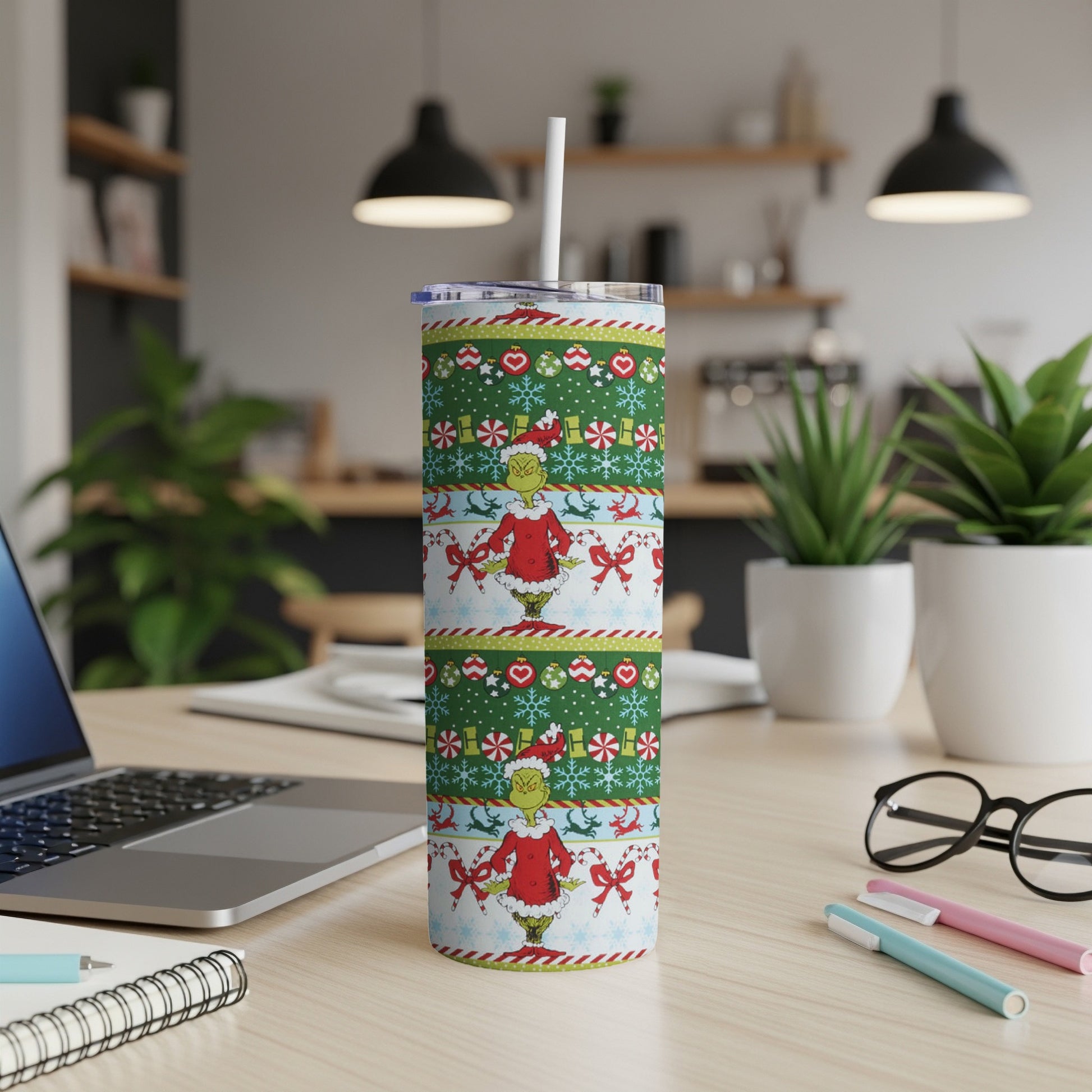 Christmas Grinch tumbler with patterned bands and straw on a desk.