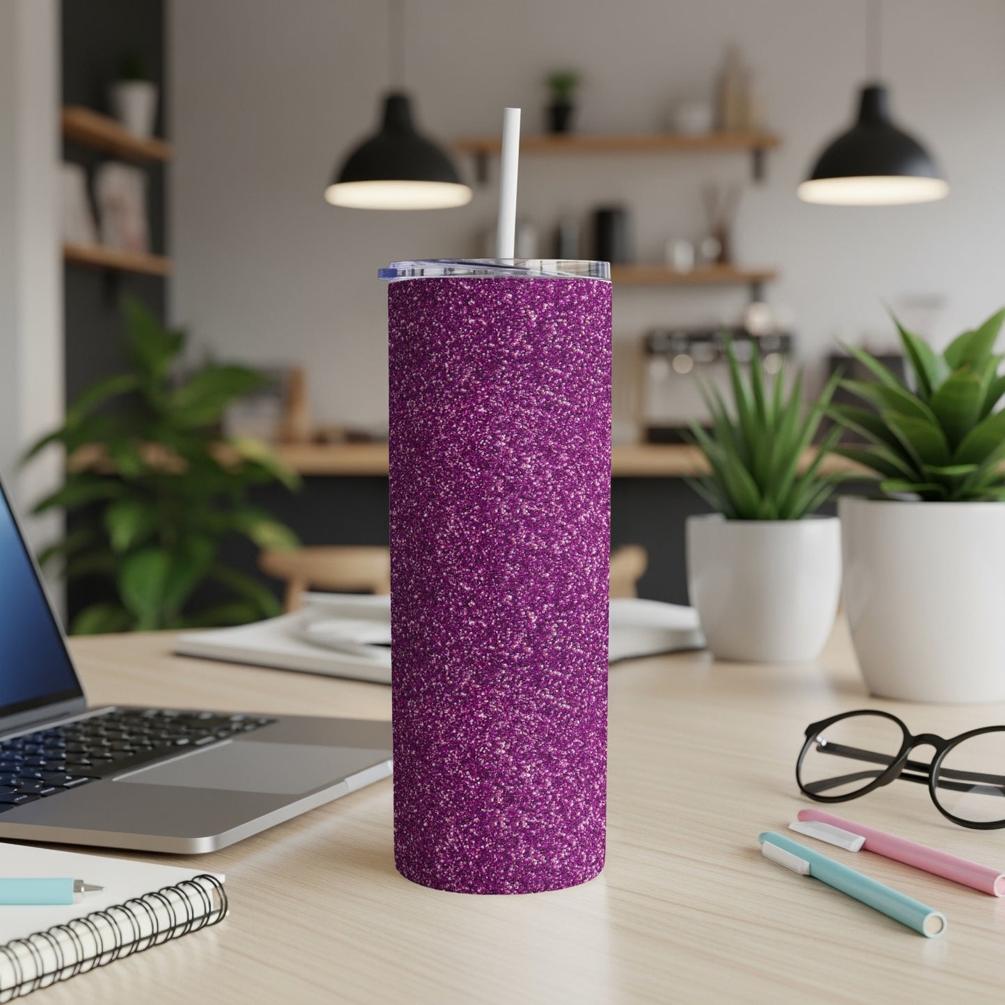 Glitter purple tumbler with straw on a desk with laptop and plants.