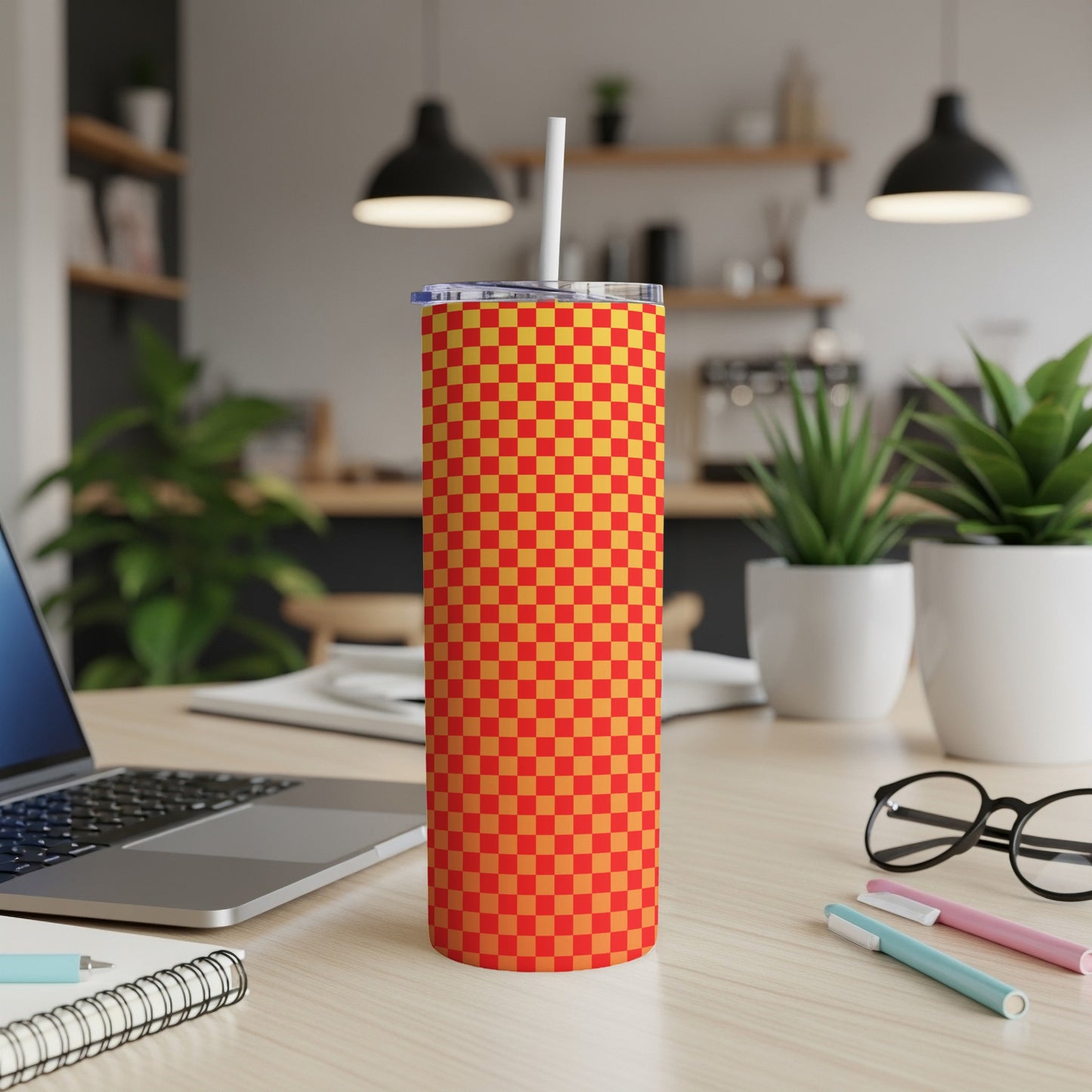 Red and orange checkered tumbler with straw on desk.