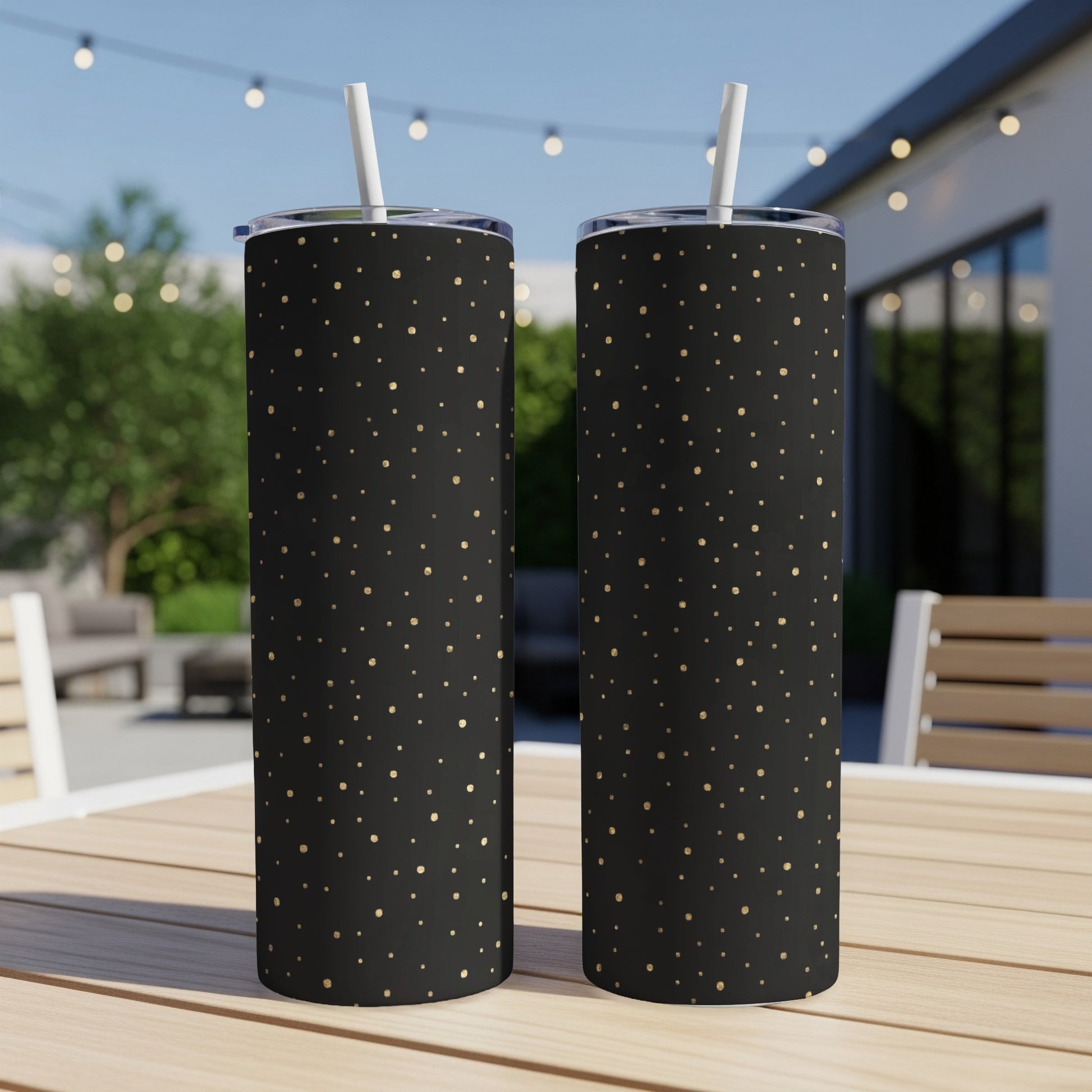 Black skinny tumblers with gold polka dots and white straws on a wooden table.