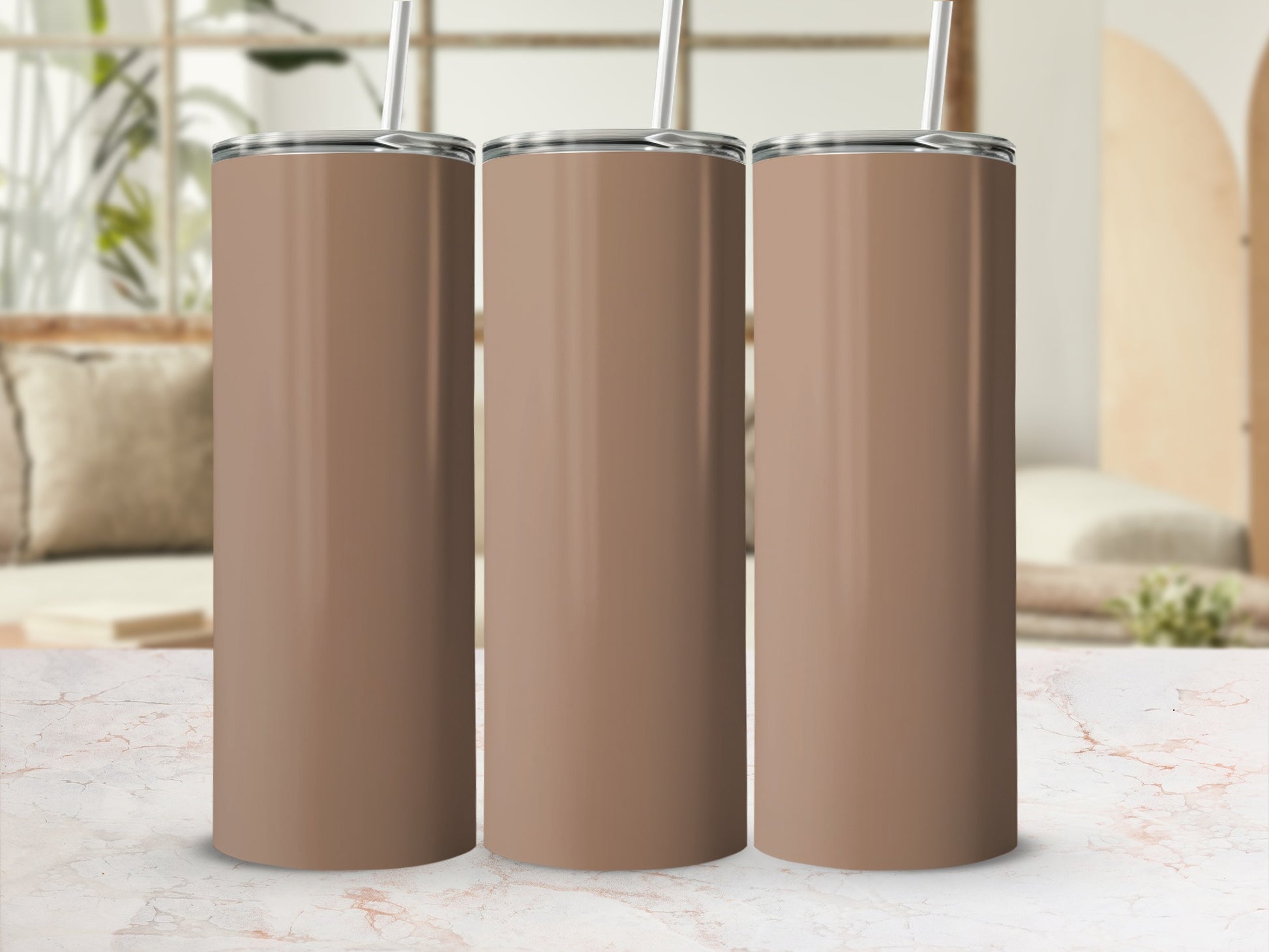 Three plain brown tumblers with straws stand on a marble countertop.