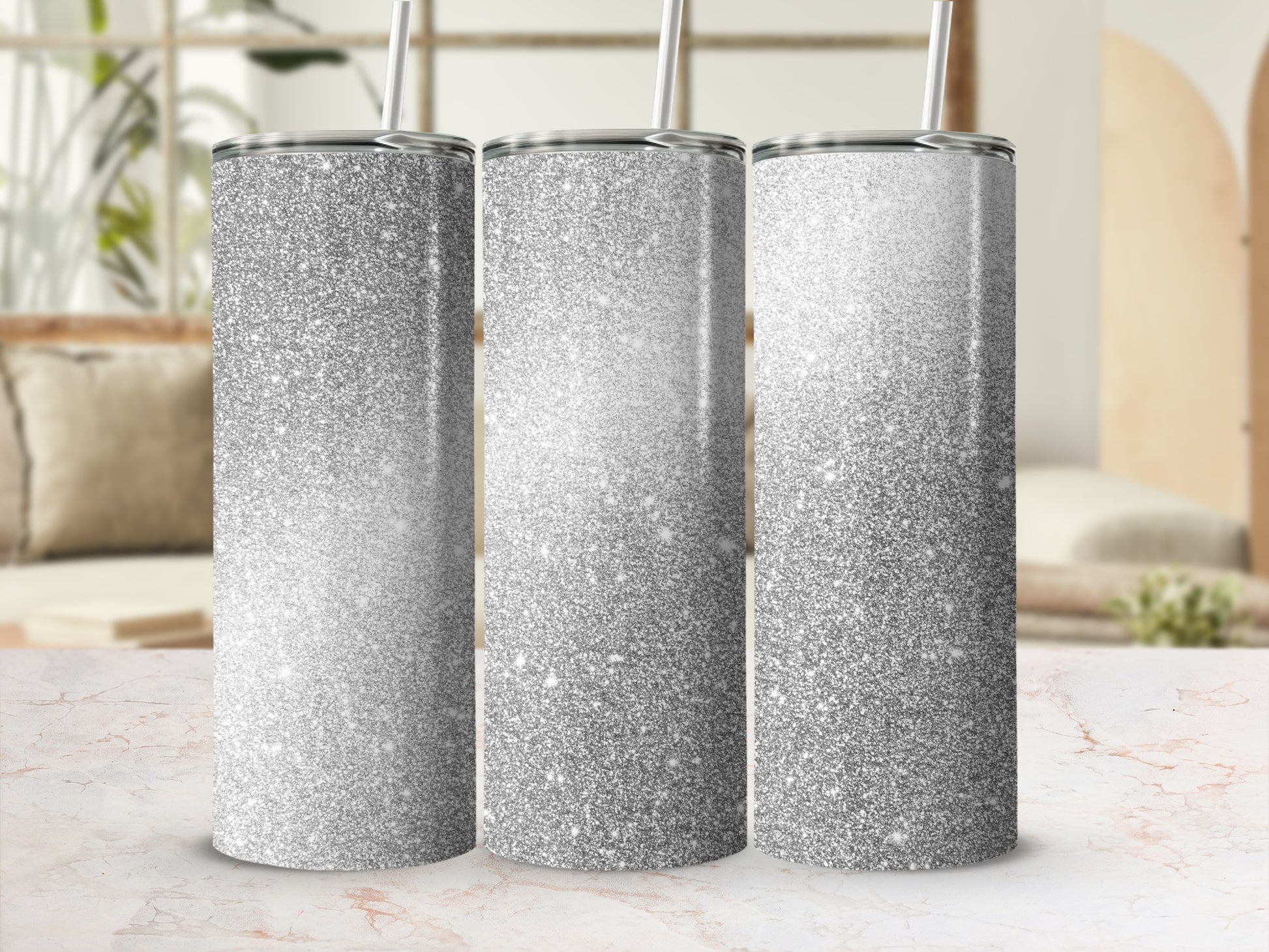 Three silver glitter tumblers with straws on a marble surface.