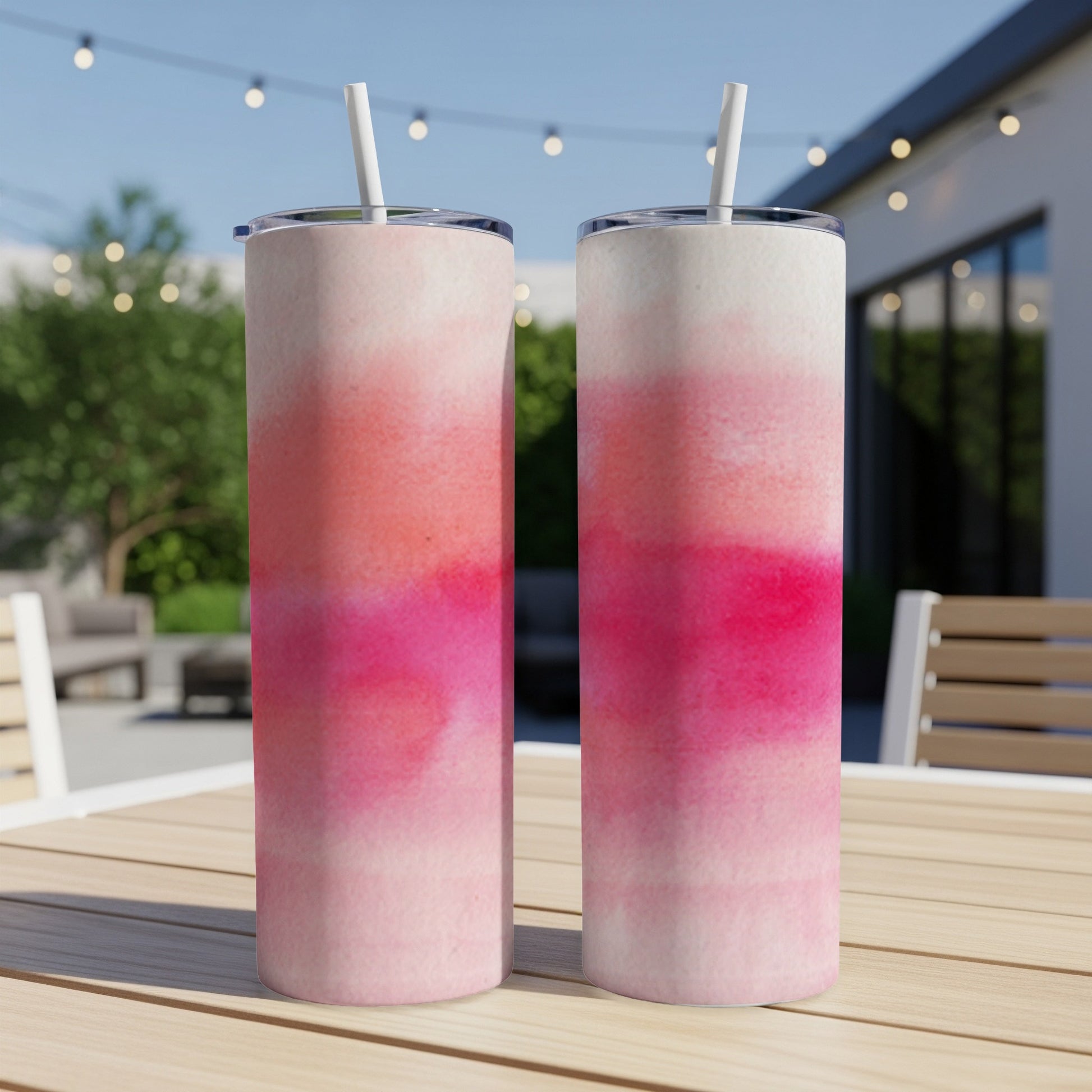 Two skinny tumblers with a pink and white ombre watercolor design sit on a table.