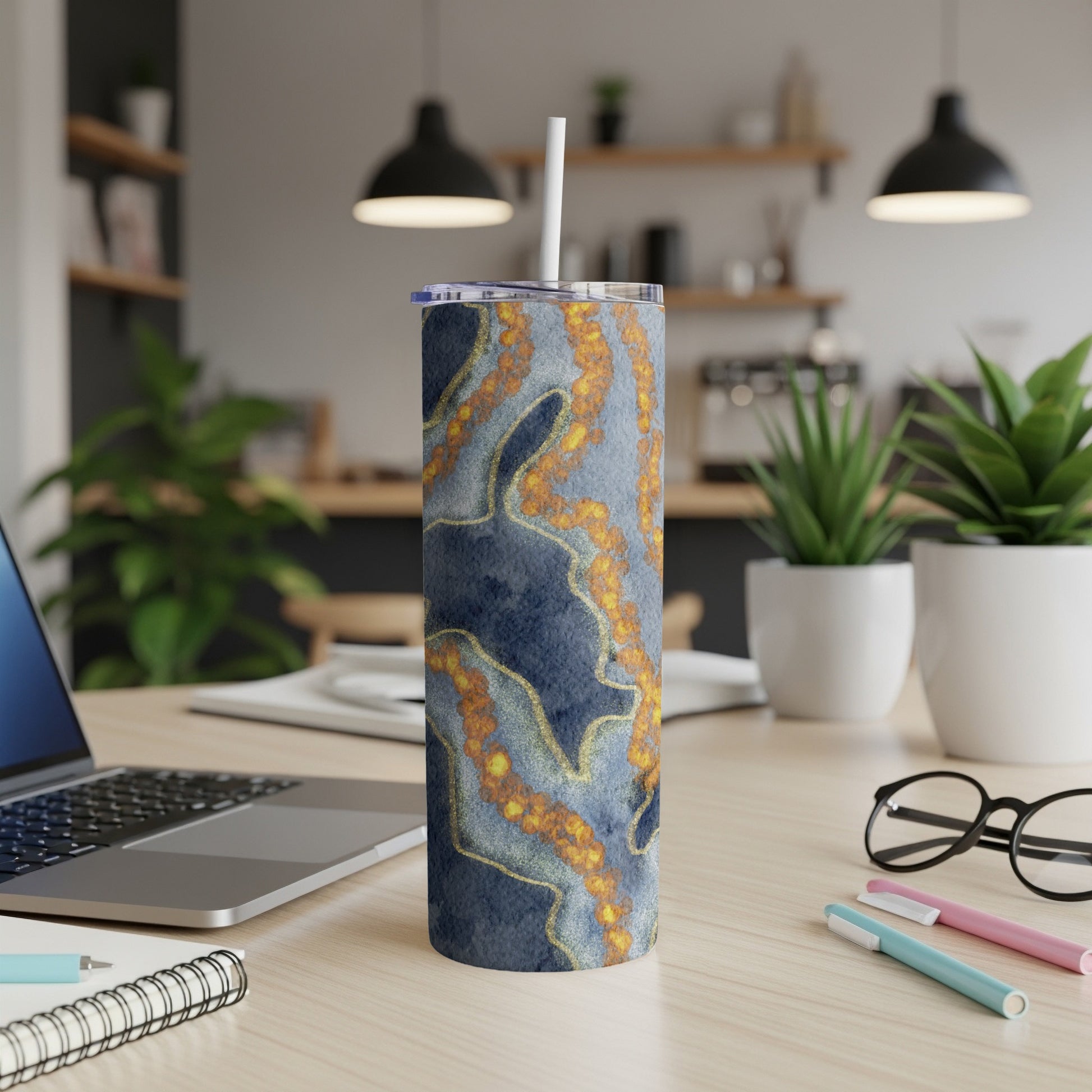 Blue and gold marbled tumbler with straw on desk.
