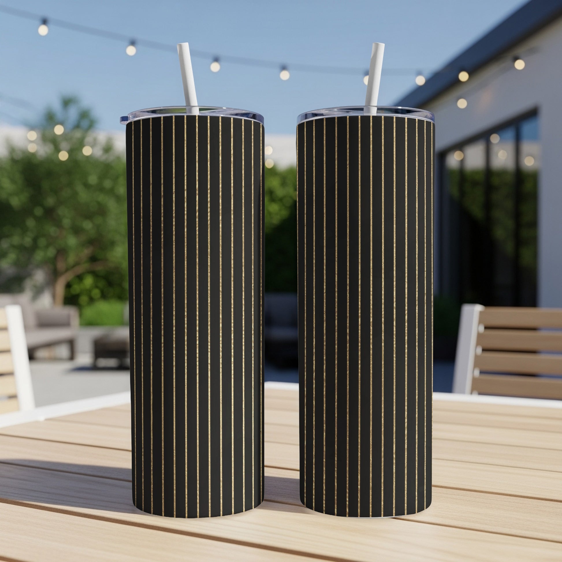 Two black tumblers with gold vertical stripes and white straws on a wooden table.